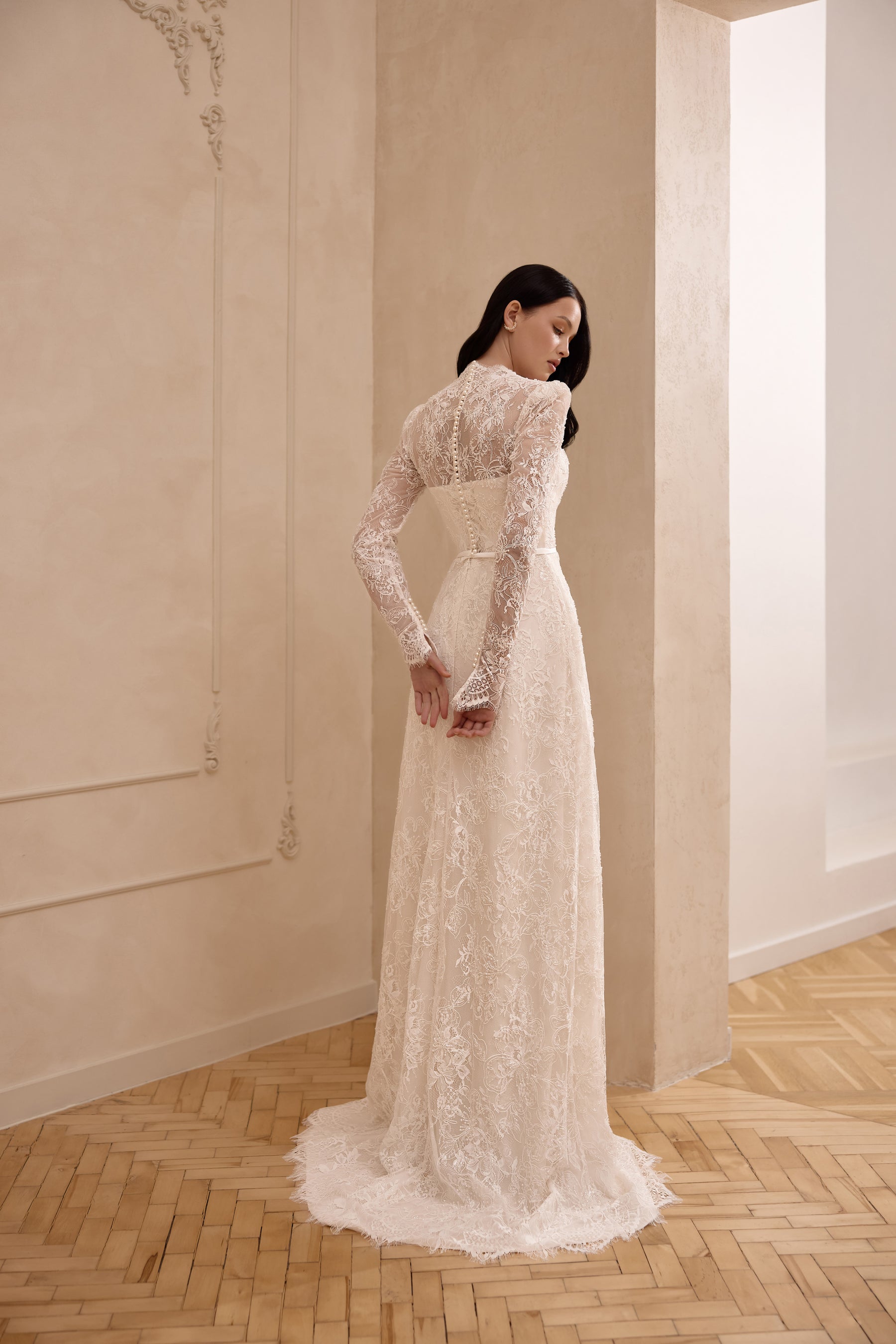 Ivory long-sleeve lace wedding dress in profile, showing its fitted sheath silhouette and scalloped train