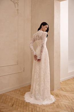 Ivory long-sleeve lace wedding dress in profile, showing its fitted sheath silhouette and scalloped train