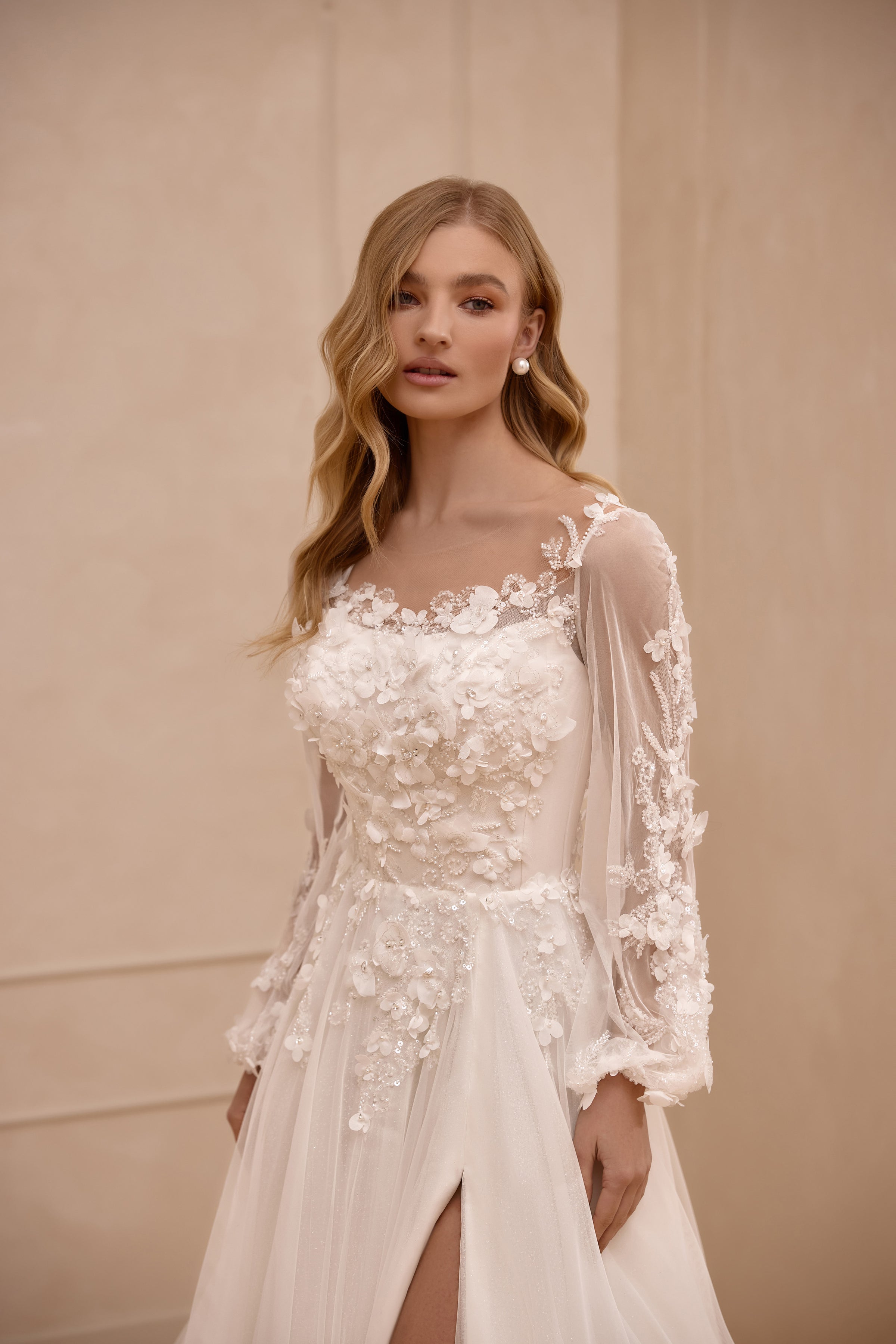 Close-up of an ivory wedding dress with a scoop neckline, sheer floral lace sleeves, and appliqué bodice