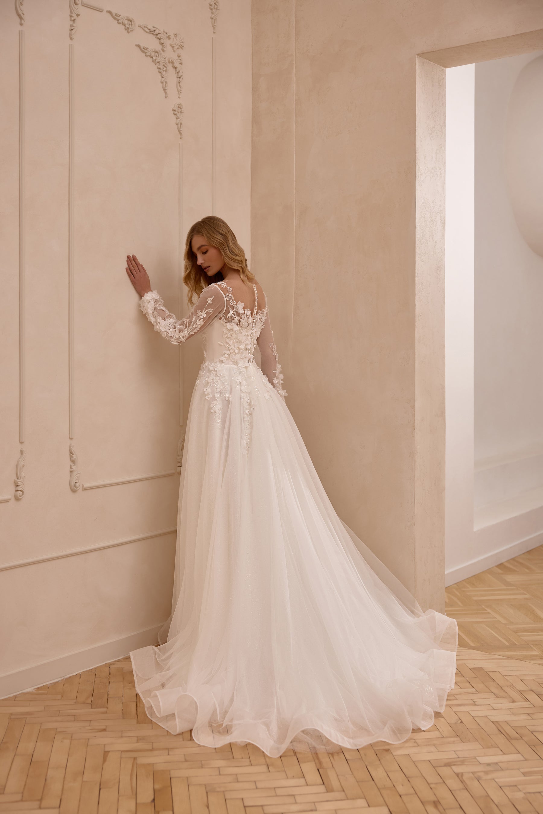 Ivory wedding dress showing a sheer floral lace back, long sleeves, flowing A-line skirt, and train