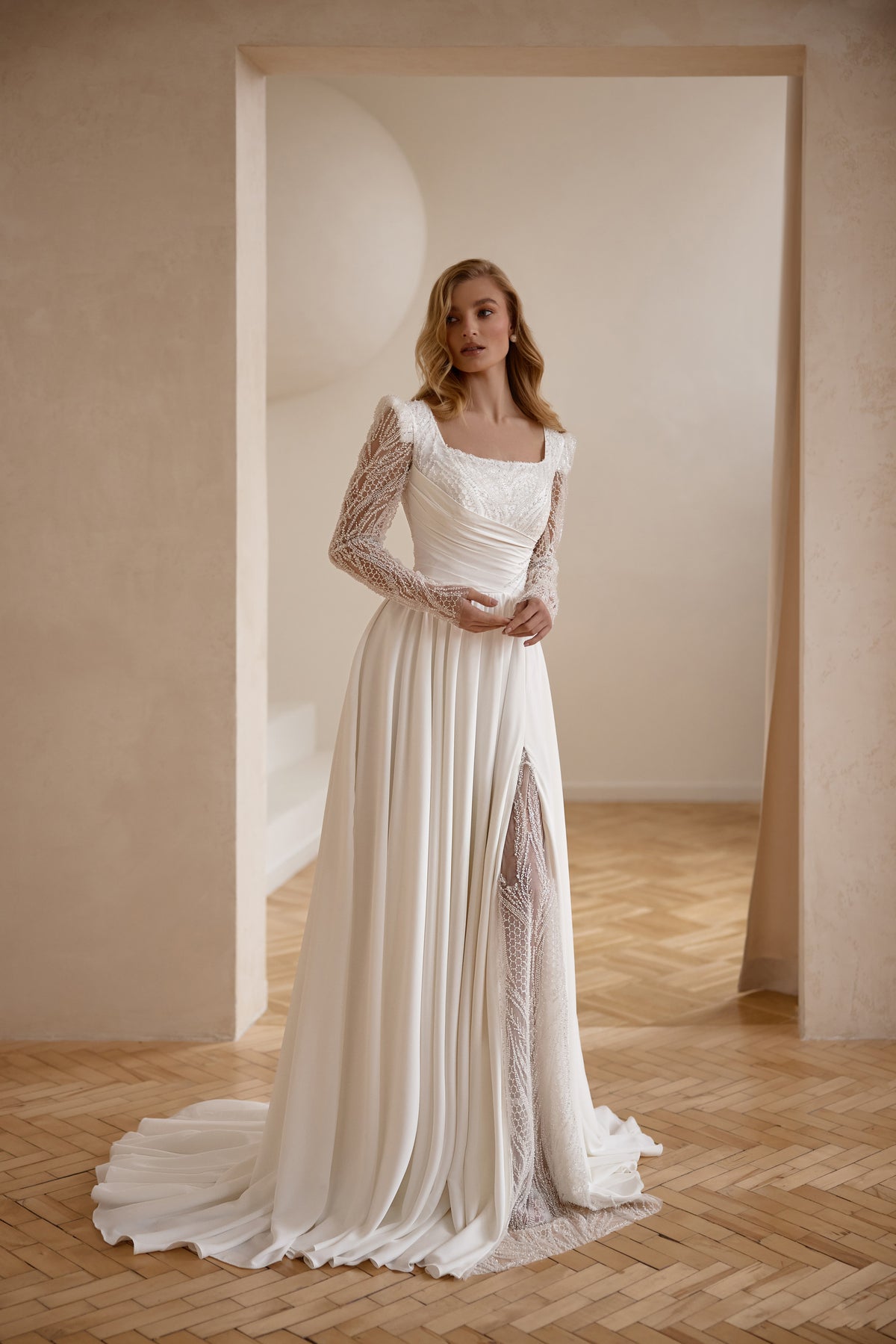Ivory A-line wedding dress with a square neckline, sheer lace sleeves, pleated skirt, and long train