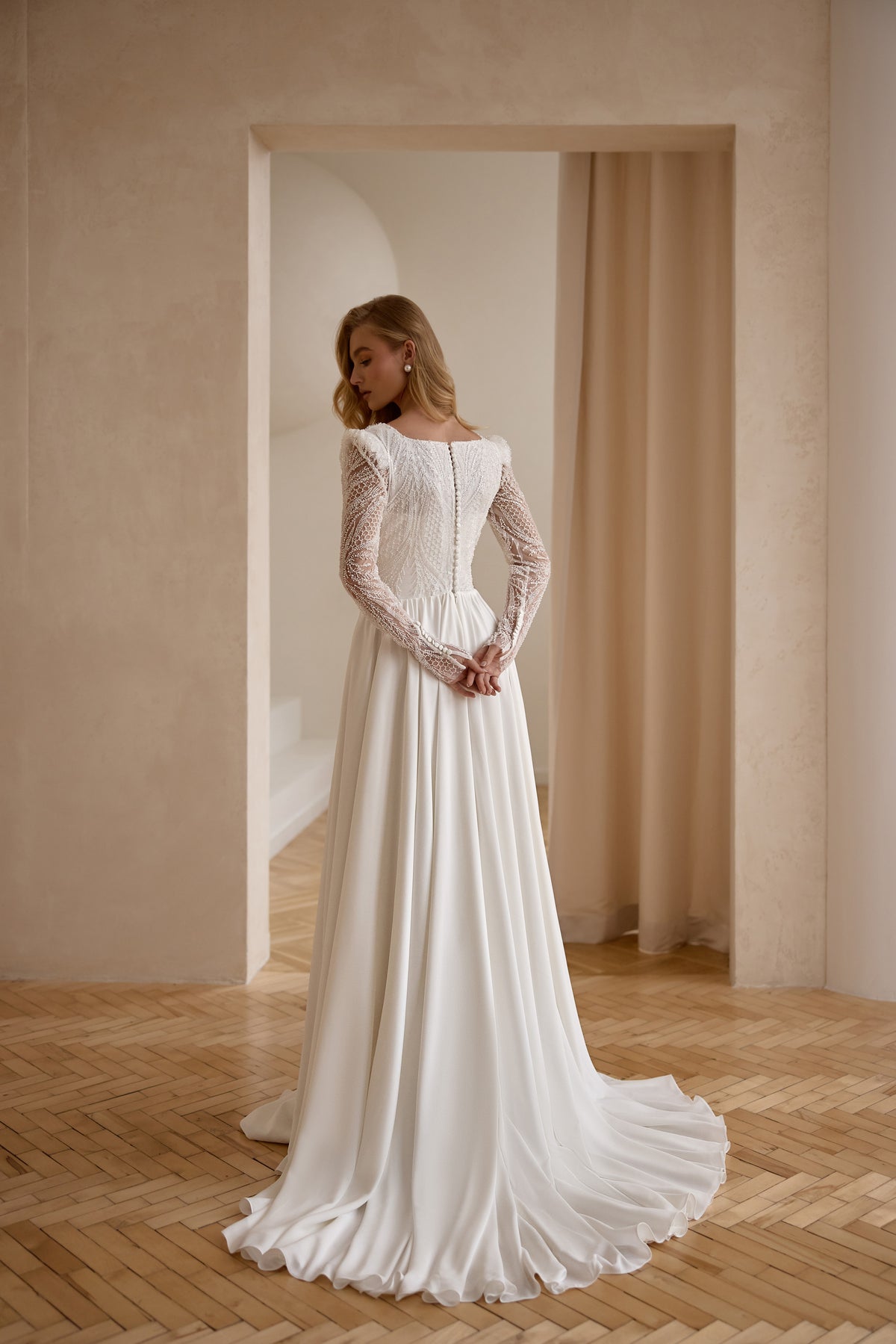 Back of an ivory wedding dress with sheer lace sleeves, a covered bodice, flowing skirt, and train