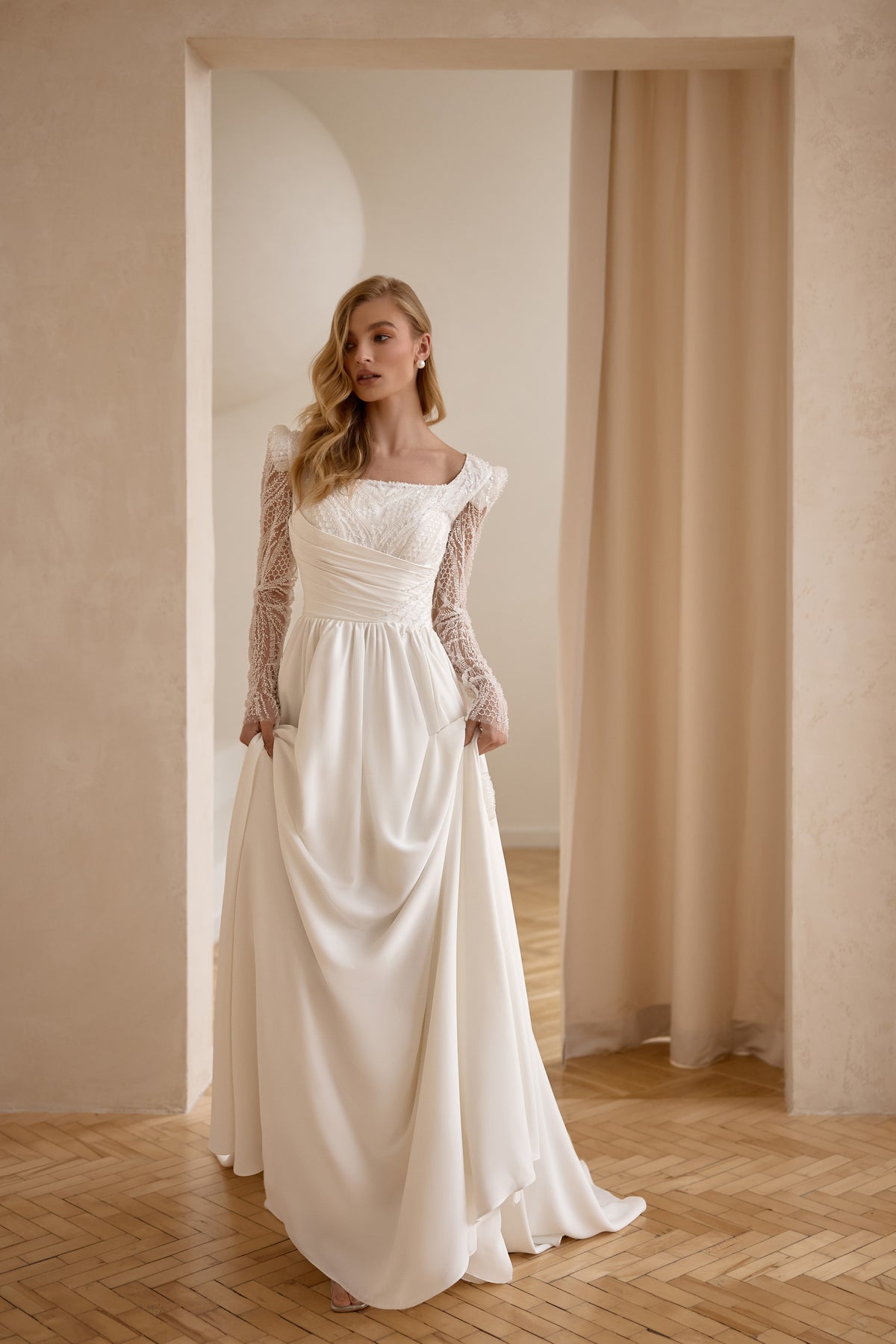 Ivory wedding dress with a square neckline, sheer lace sleeves, ruched waist, and draped satin skirt