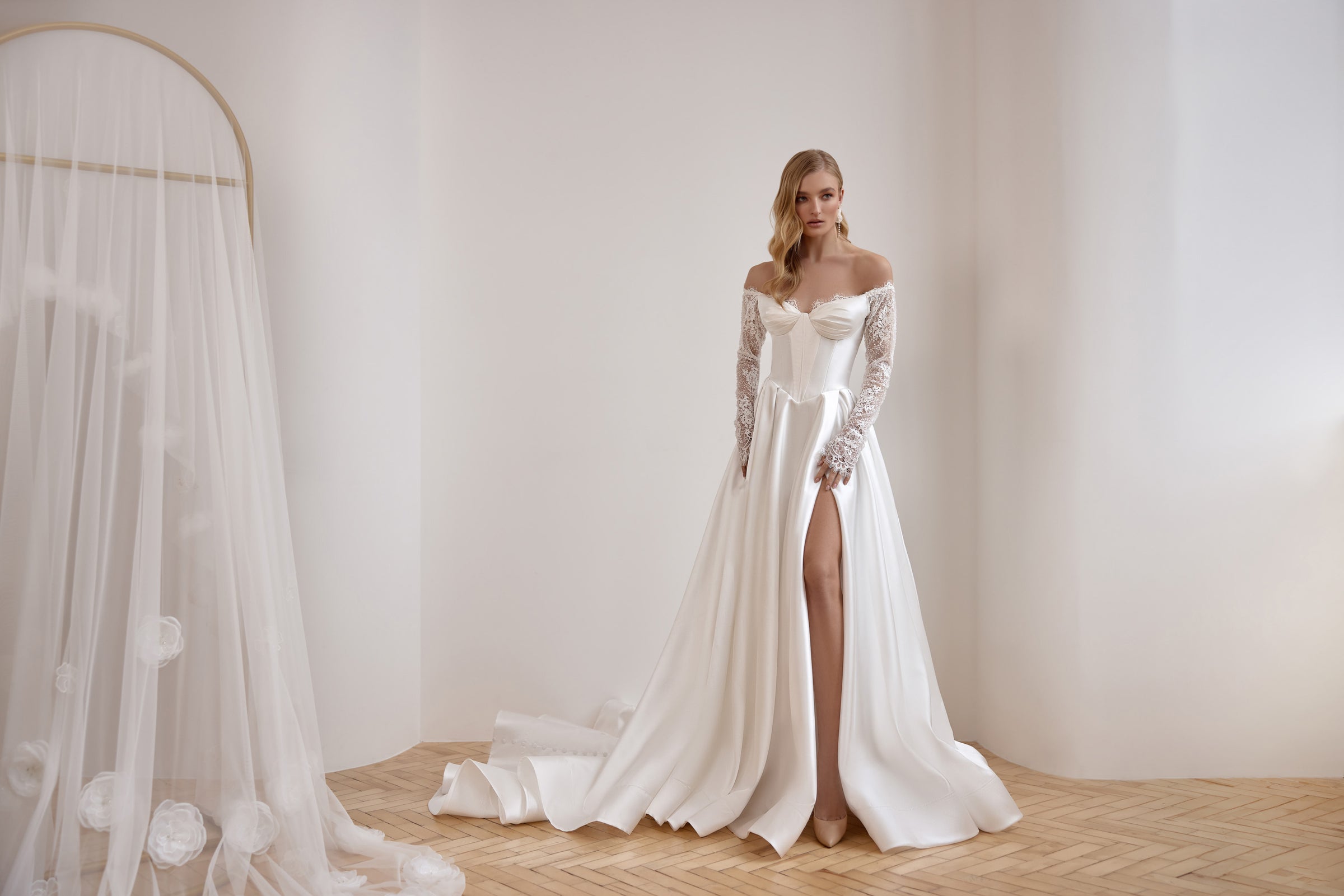 Flowing ivory wedding dress with long lace sleeves, an off-the-shoulder neckline, front slit, and train