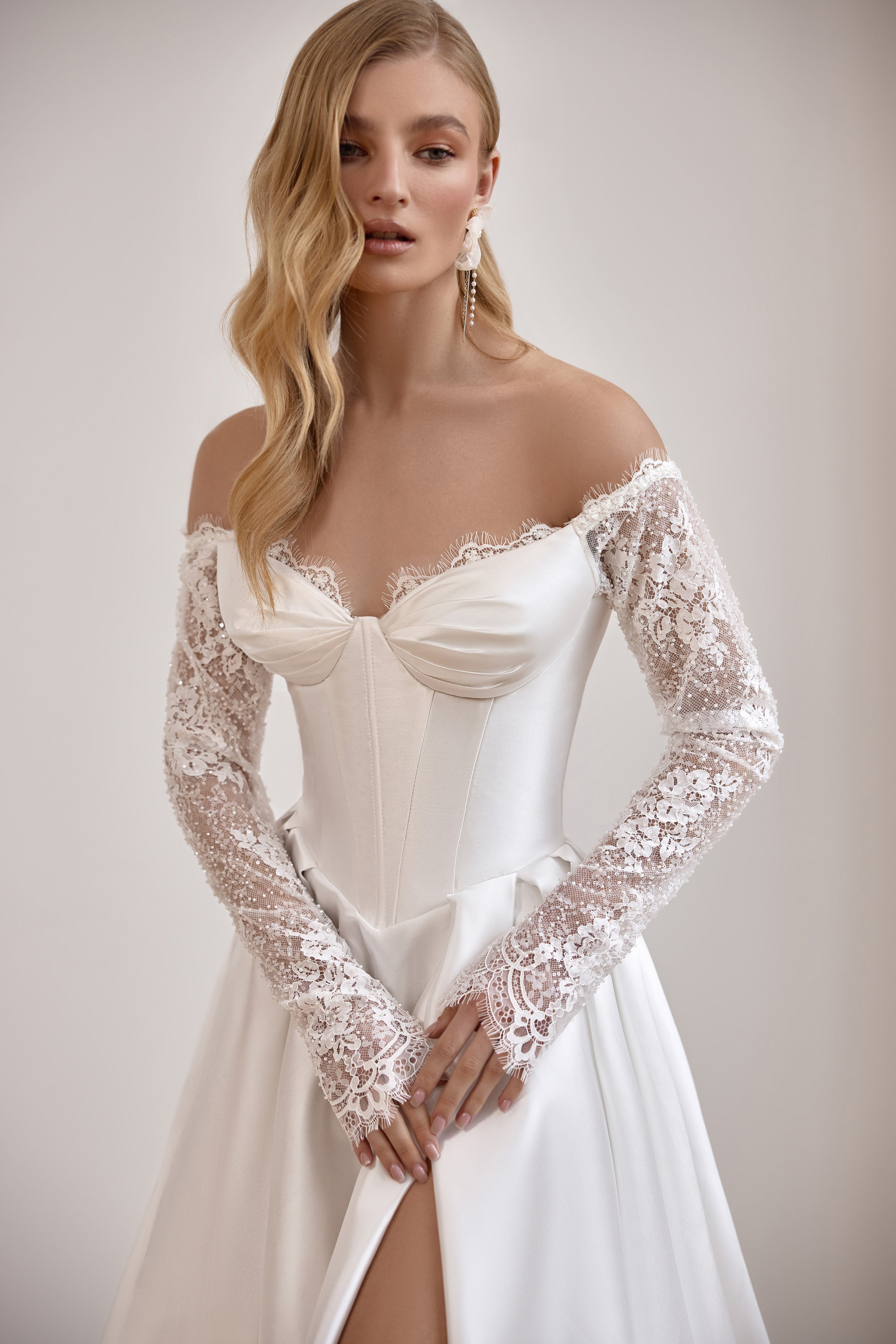 Close-up of an ivory wedding dress bodice with gathered neckline, floral lace sleeves, and front slit