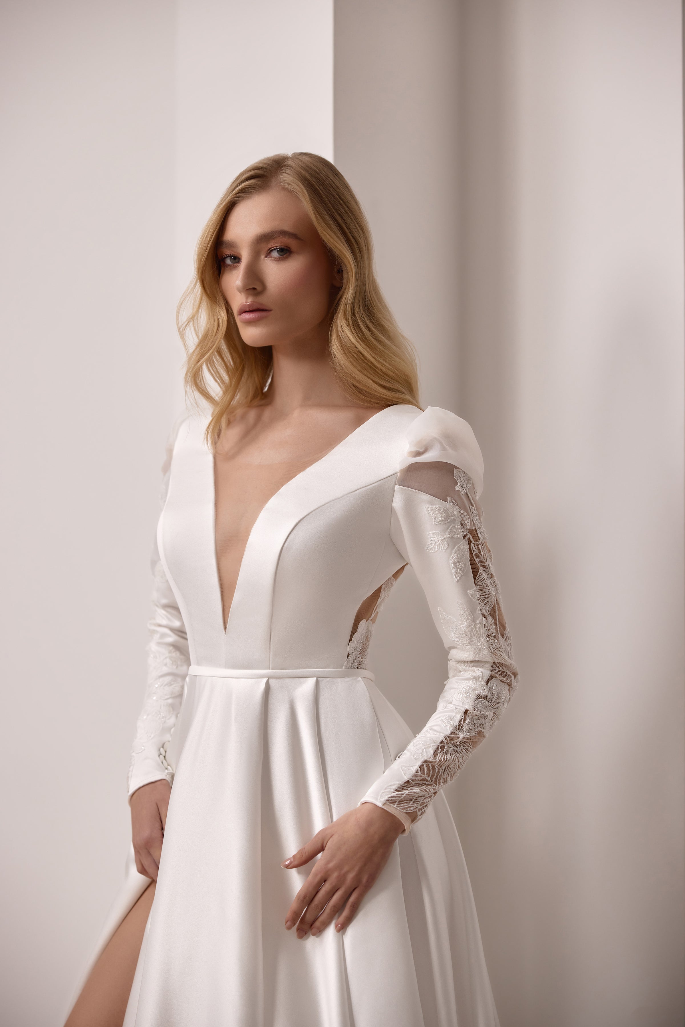 Ivory wedding dress with a plunging V-neckline, fitted lace sleeves, and a satin A-line skirt with slit