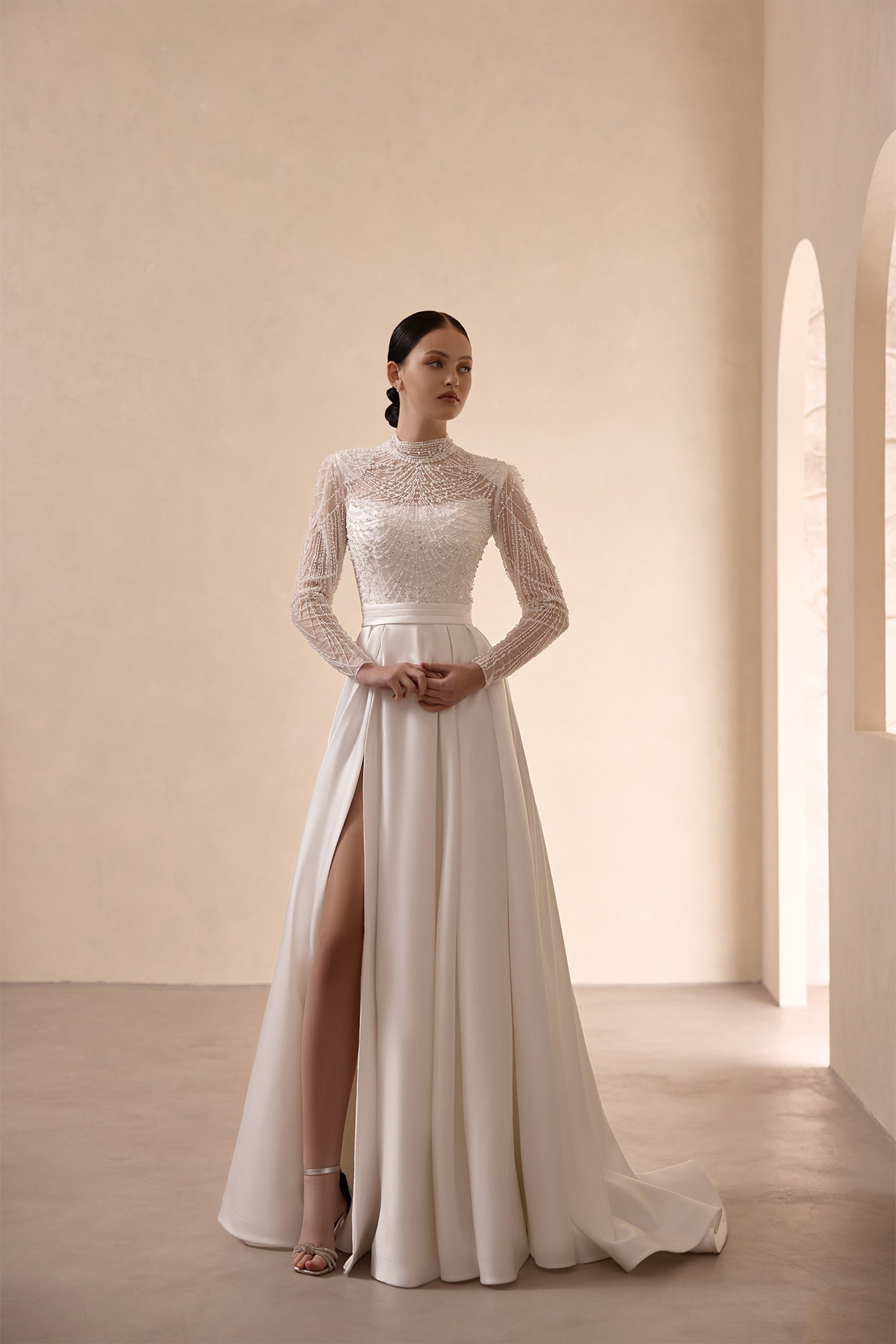 Ivory A-line wedding dress with a high beaded neckline, long sleeves, waist sash, and thigh-high slit