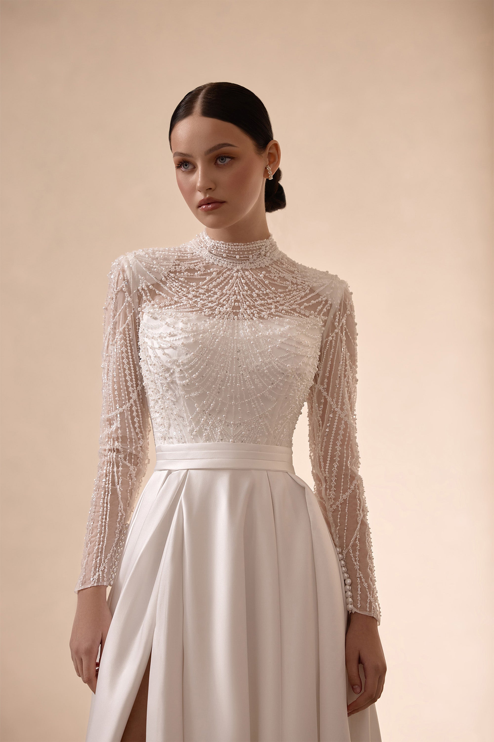 Close-up of intricate beaded long sleeves and high neckline on an ivory satin wedding dress