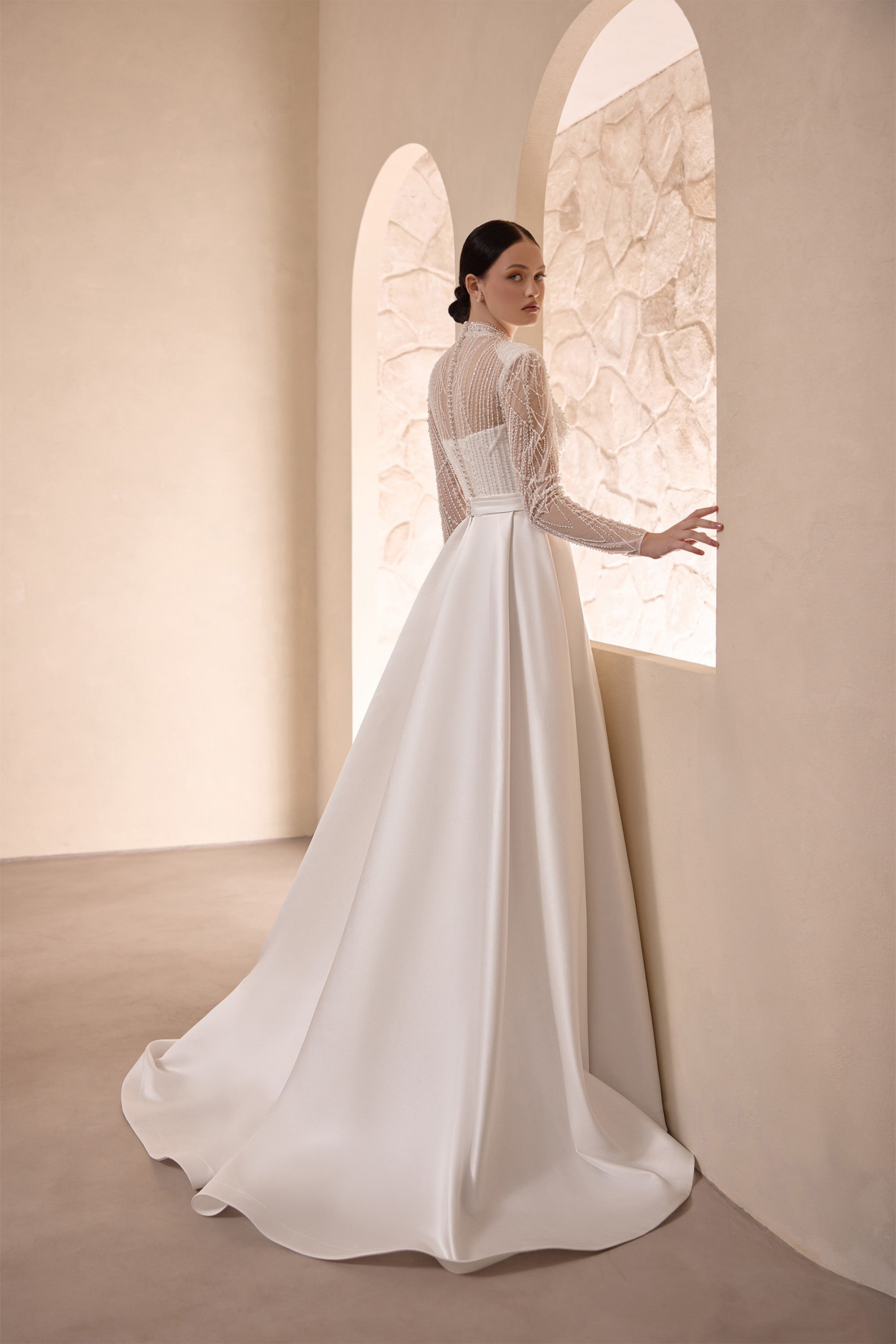 Back view of an ivory wedding dress with a beaded long-sleeve bodice and sweeping satin train