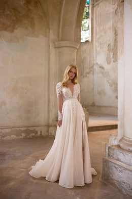 Deep V-neck ivory wedding dress with long floral-lace sleeves, a flowing A-line skirt, and subtle sparkle