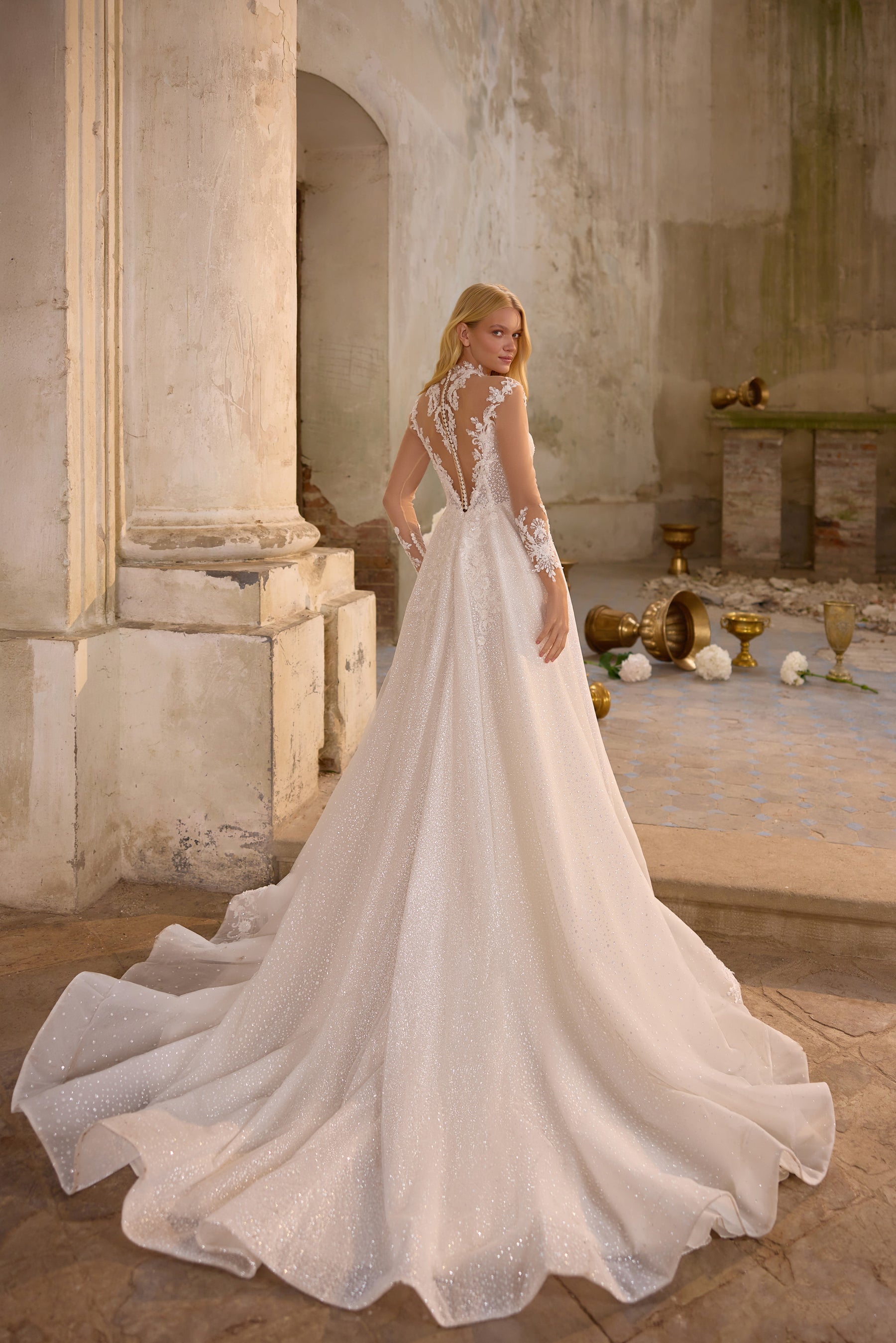 Sparkling ivory A-line wedding dress with sheer lace sleeves and a wide, flowing cathedral-length train