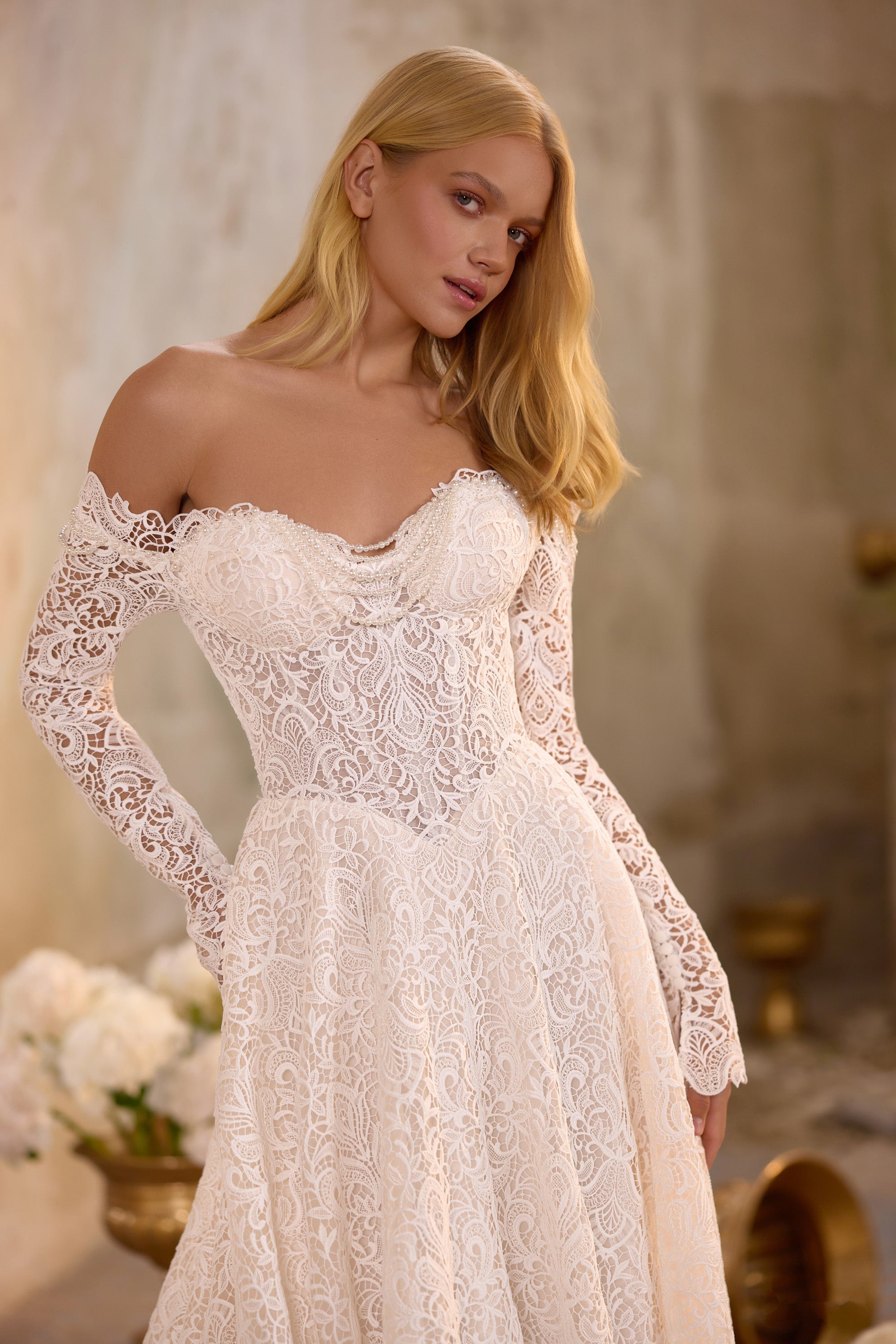 Close-up of an ivory wedding dress bodice with floral lace, off-the-shoulder neckline, and long sleeves