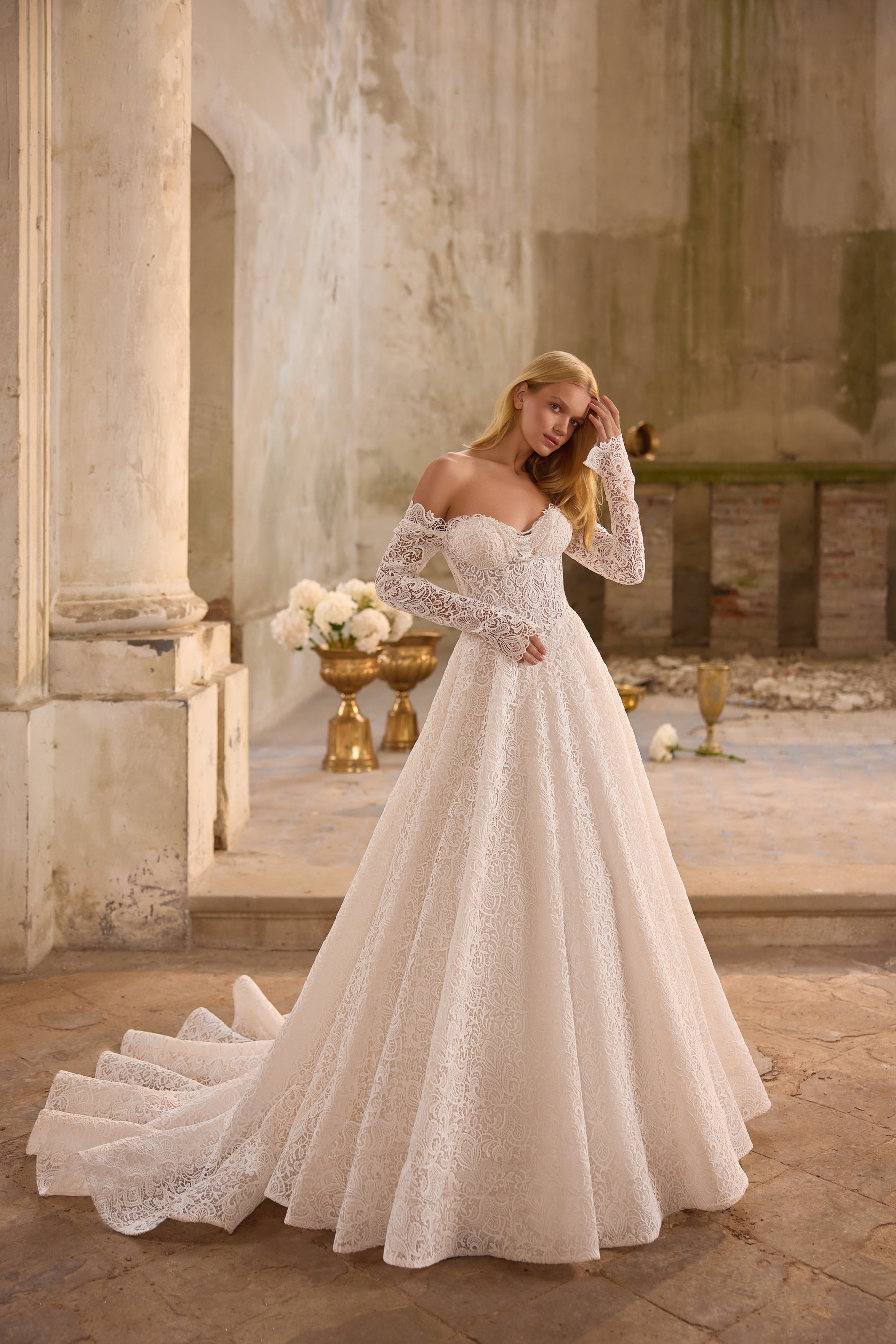 Ivory wedding dress with an off-the-shoulder lace neckline, fitted bodice, long sleeves, and train