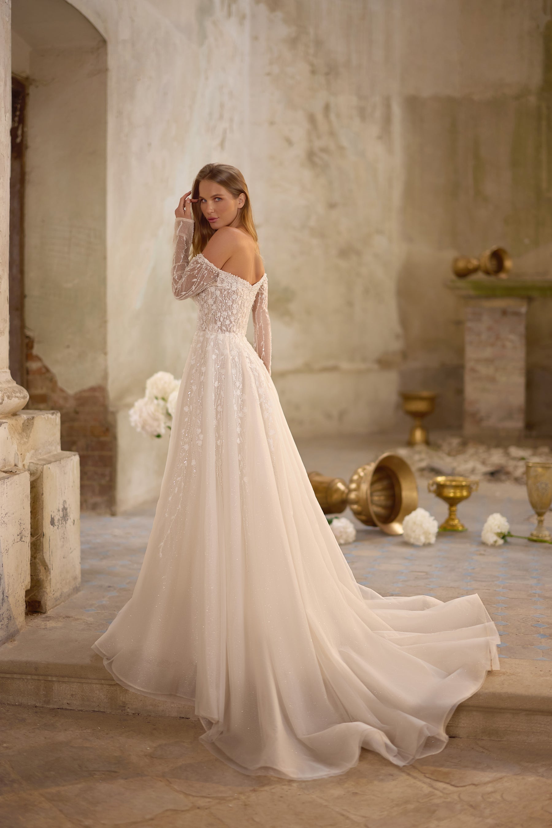 Ivory wedding dress shown from the back with sheer lace sleeves, an A-line skirt, and a long flowing train