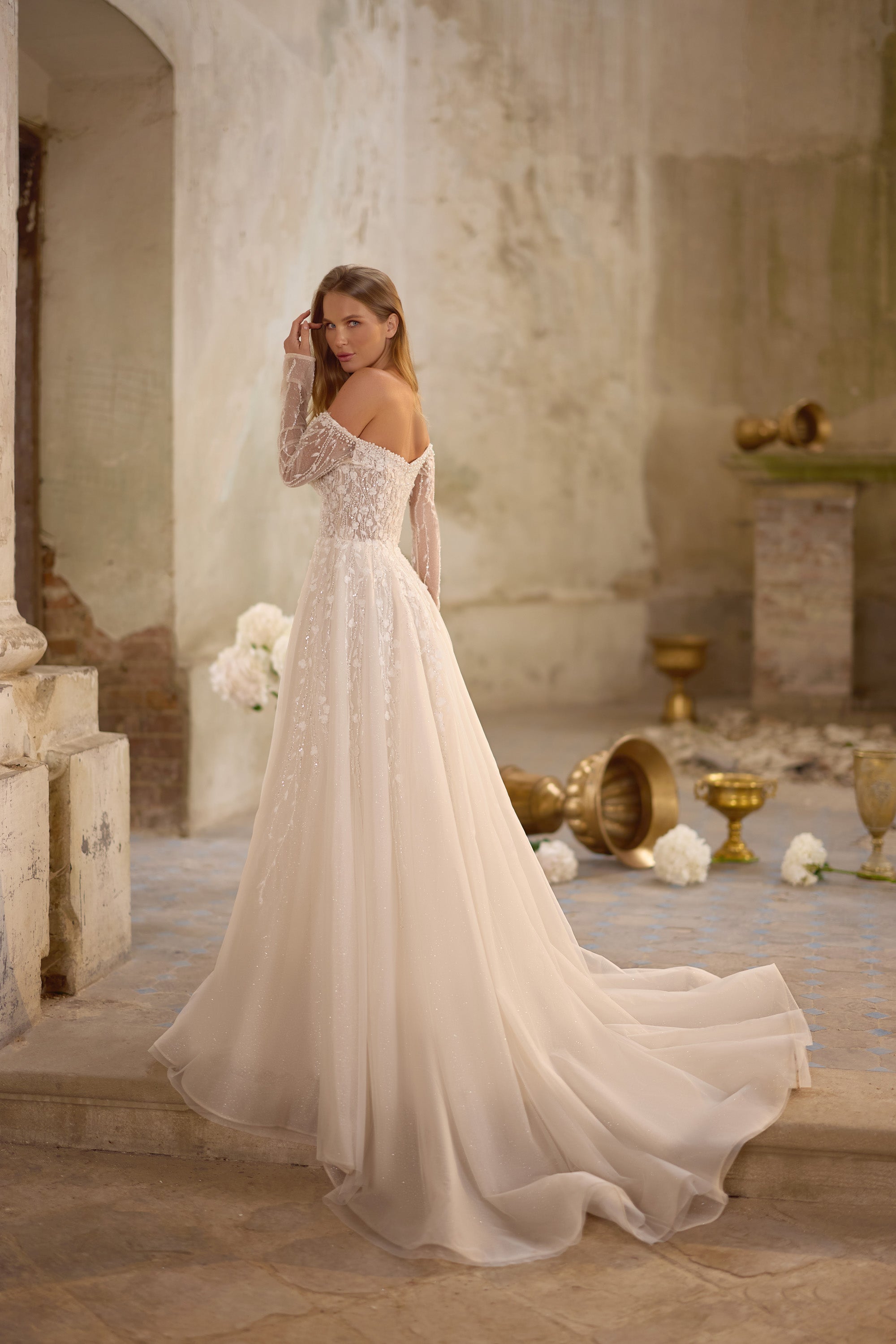 Ivory wedding dress shown from the back with sheer lace sleeves, an A-line skirt, and a long flowing train
