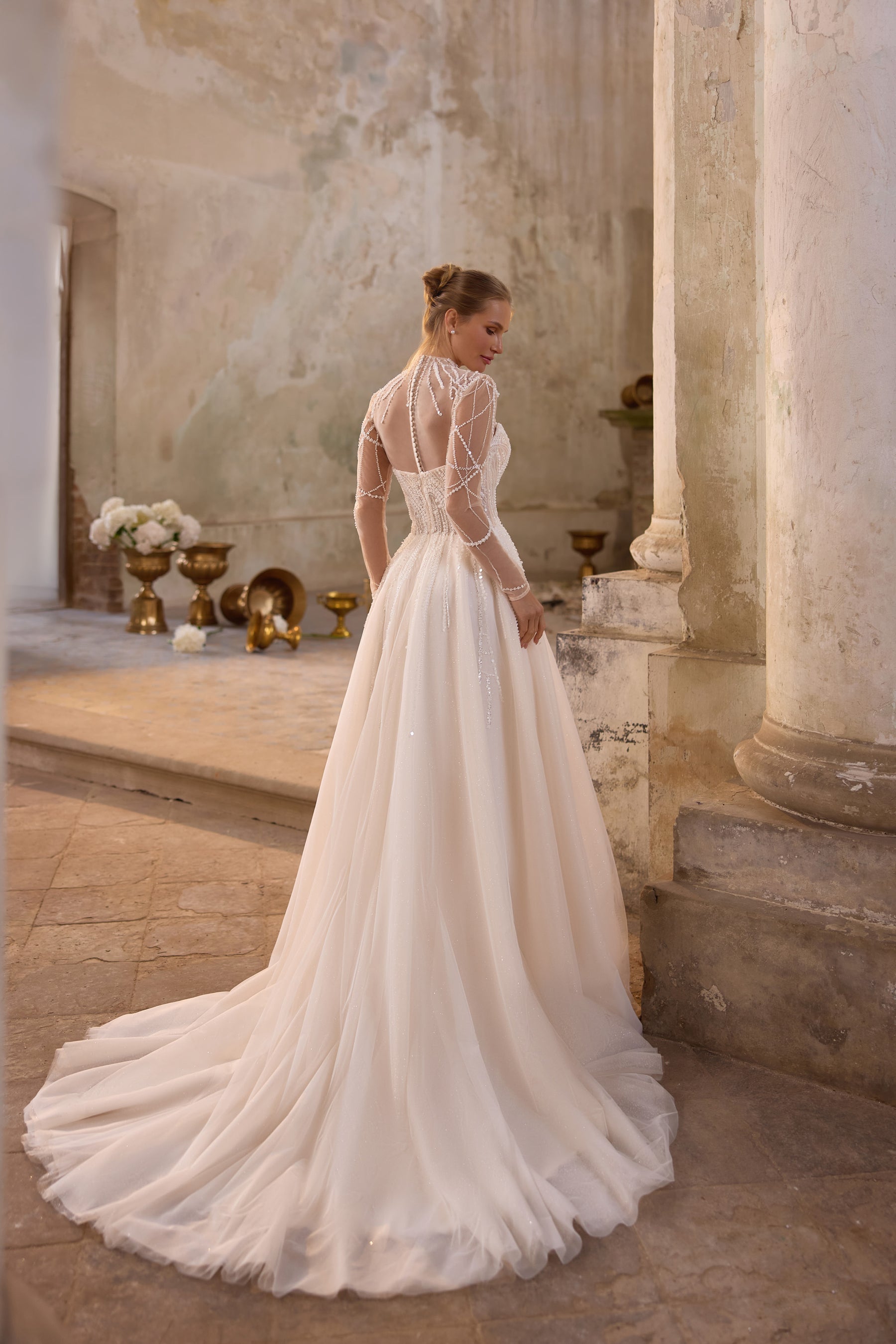 Back of an ivory wedding dress with beaded illusion sleeves, sheer back, and a long flowing train