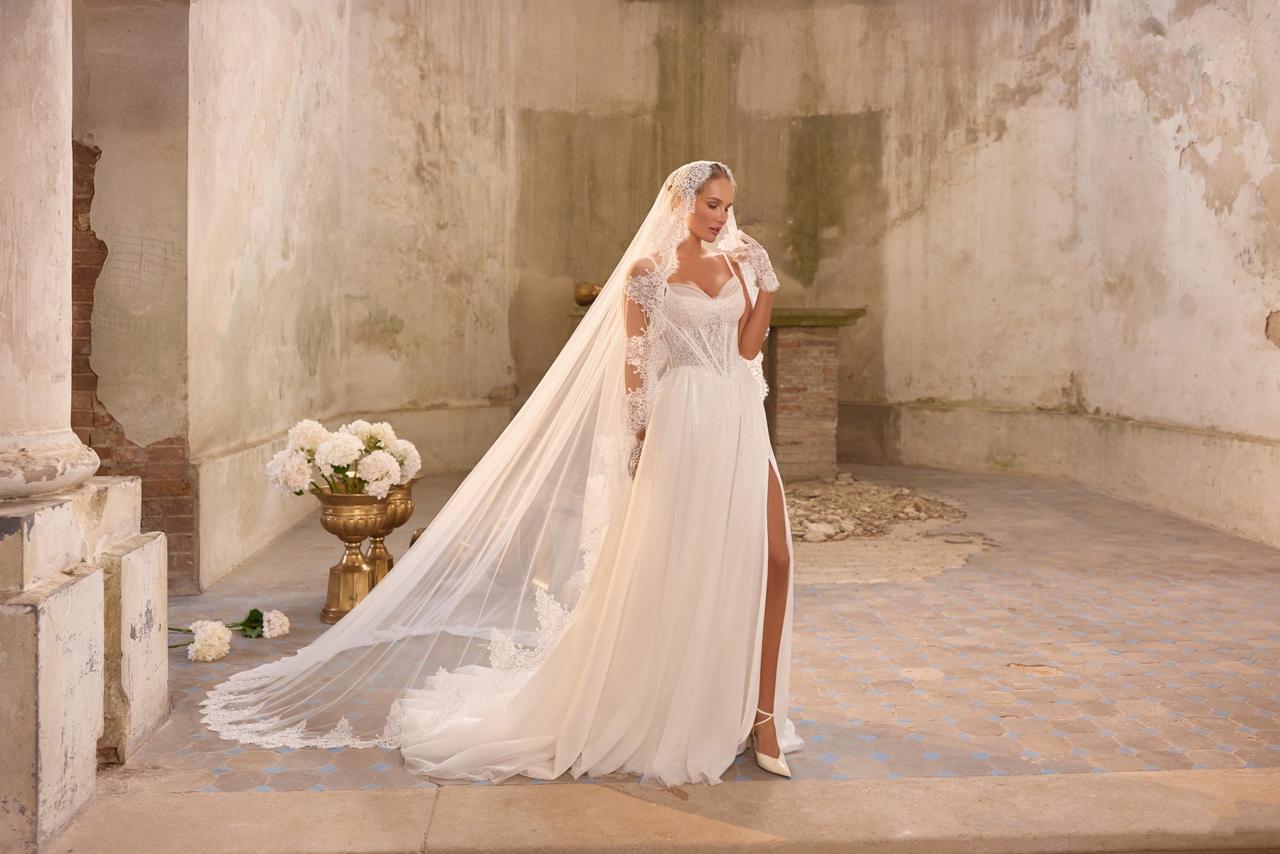 Full-length ivory wedding dress with a sheer lace-edged veil, side slit, and long flowing train