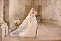 Full-length ivory wedding dress with a sheer lace-edged veil, side slit, and long flowing train