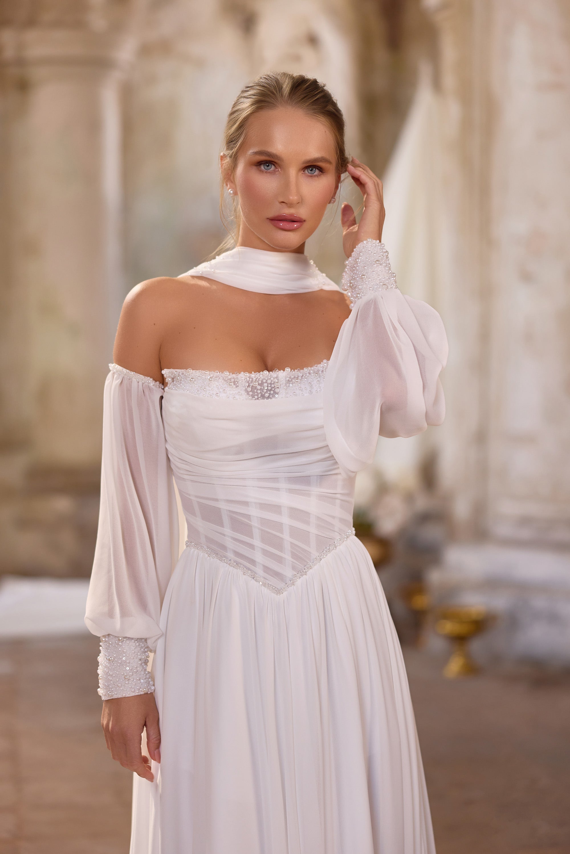 Close-up of an ivory wedding dress with a ruched bodice, beaded neckline, sheer sleeves, and sparkling cuffs