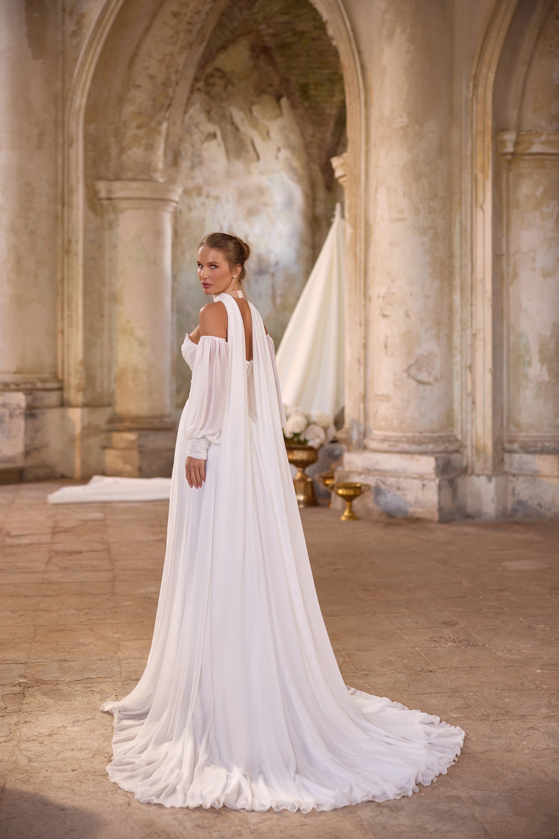 Three-quarter back view of an ivory wedding dress with a flowing detachable cape and long gathered train