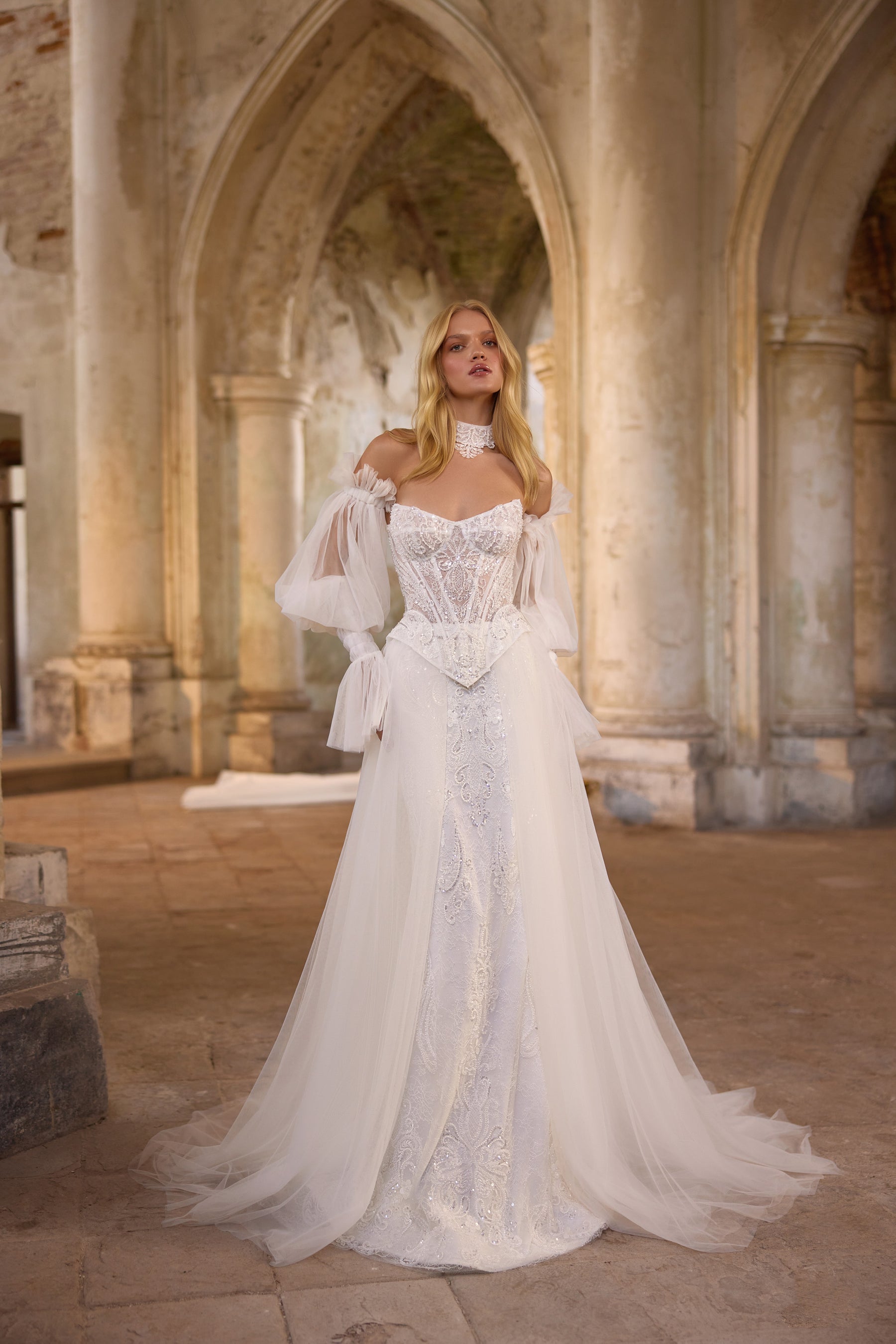 Ivory wedding dress with a beaded sweetheart bodice, sheer puff sleeves, and a flowing overskirt