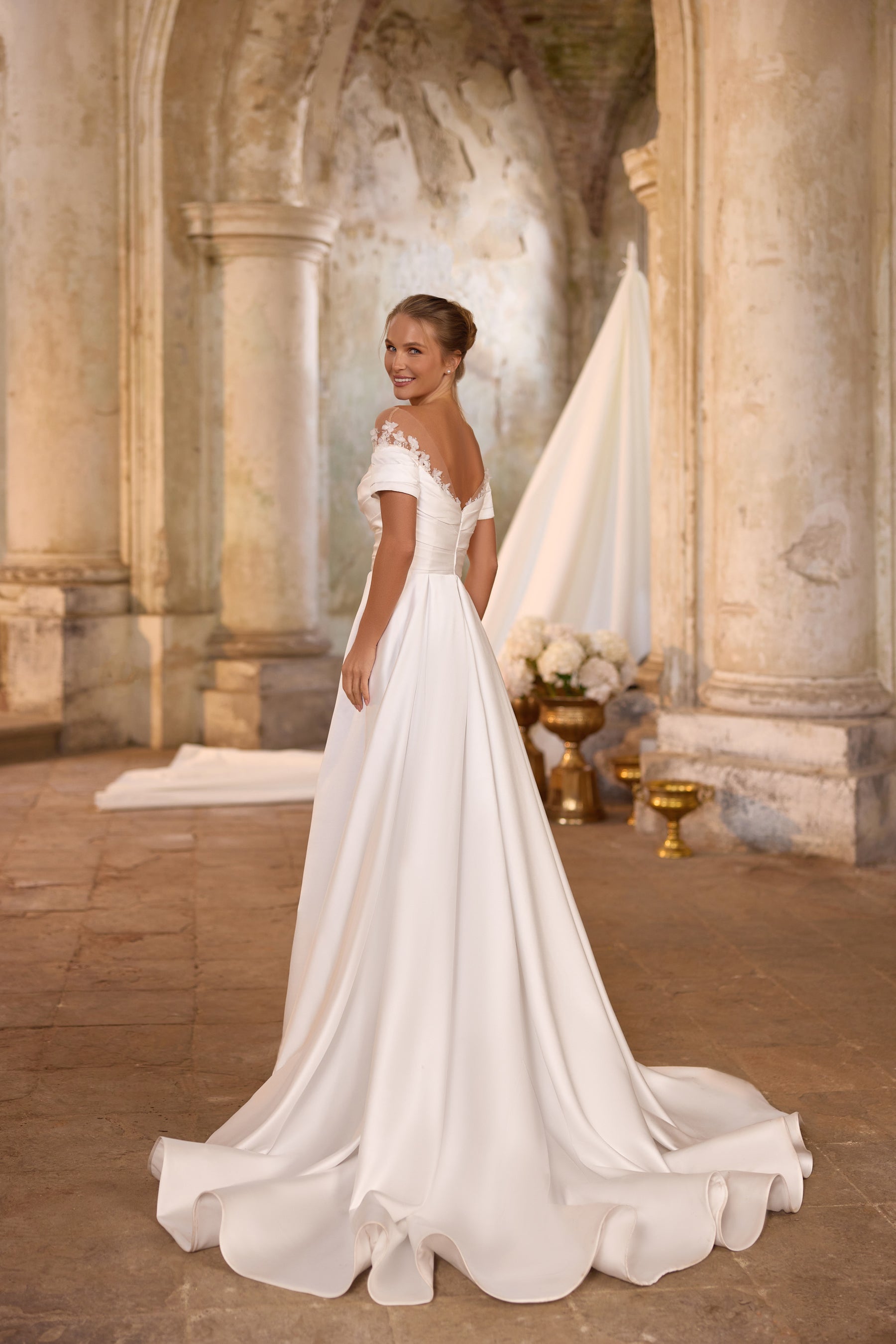 Ivory wedding dress with an off-shoulder neckline, short sleeves, fitted waist, and flowing A-line train