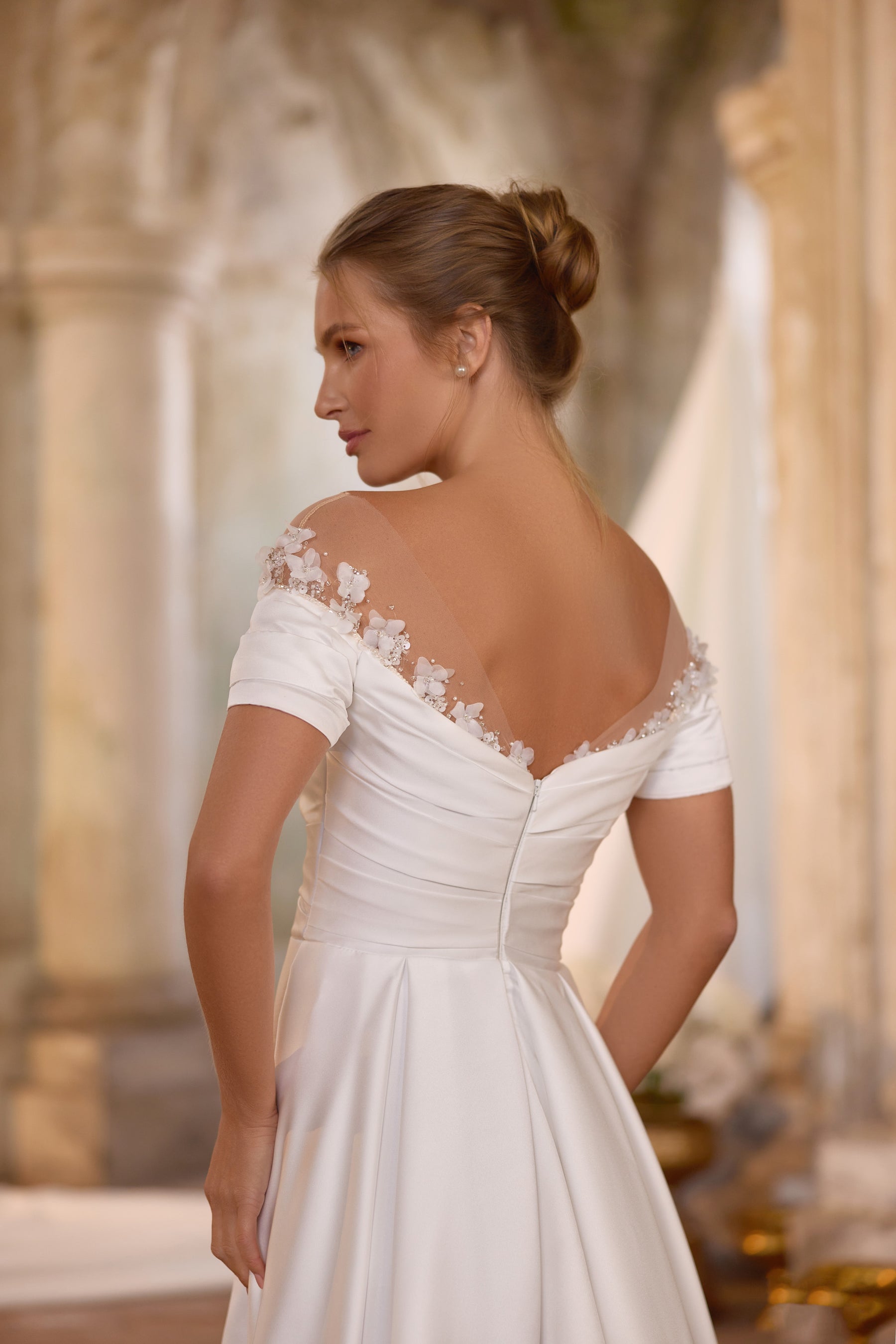 Ivory wedding dress showing a sheer floral-lace back yoke, ruched waist, short sleeves, and flowing skirt