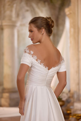 Ivory wedding dress showing a sheer floral-lace back yoke, ruched waist, short sleeves, and flowing skirt