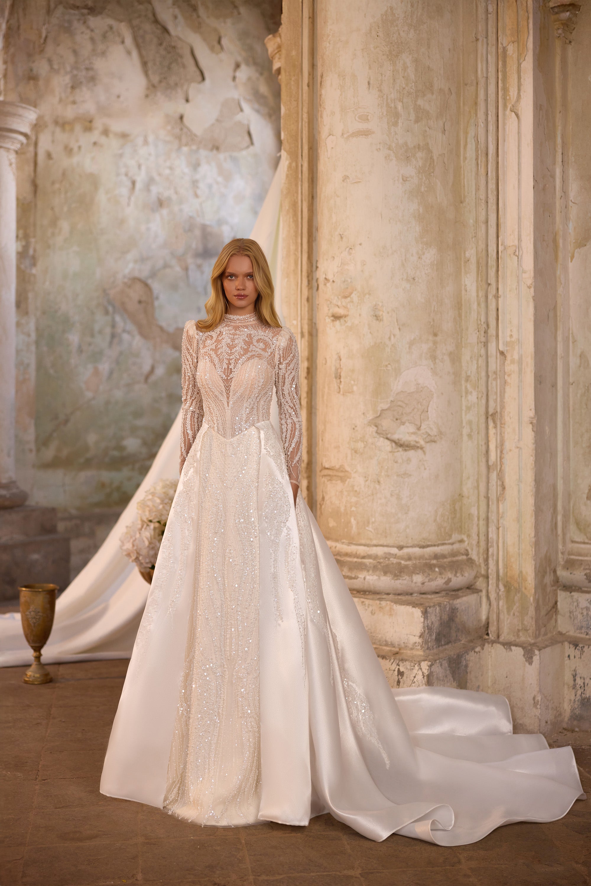 Ivory wedding dress shown with a detachable full overskirt, long lace sleeves, and a beaded high neckline