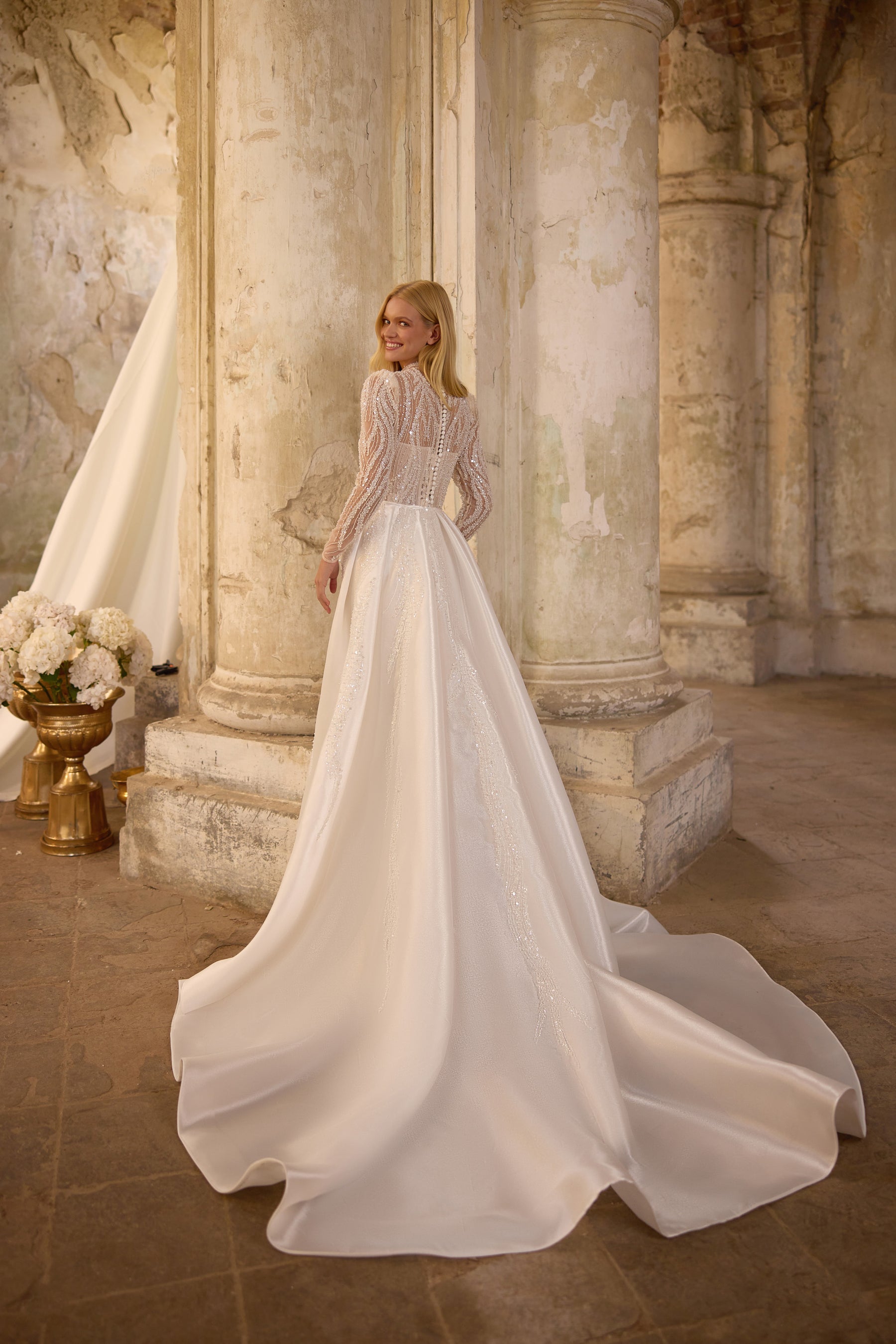 Rear view of an ivory wedding dress with a detachable full overskirt and a wide, flowing train