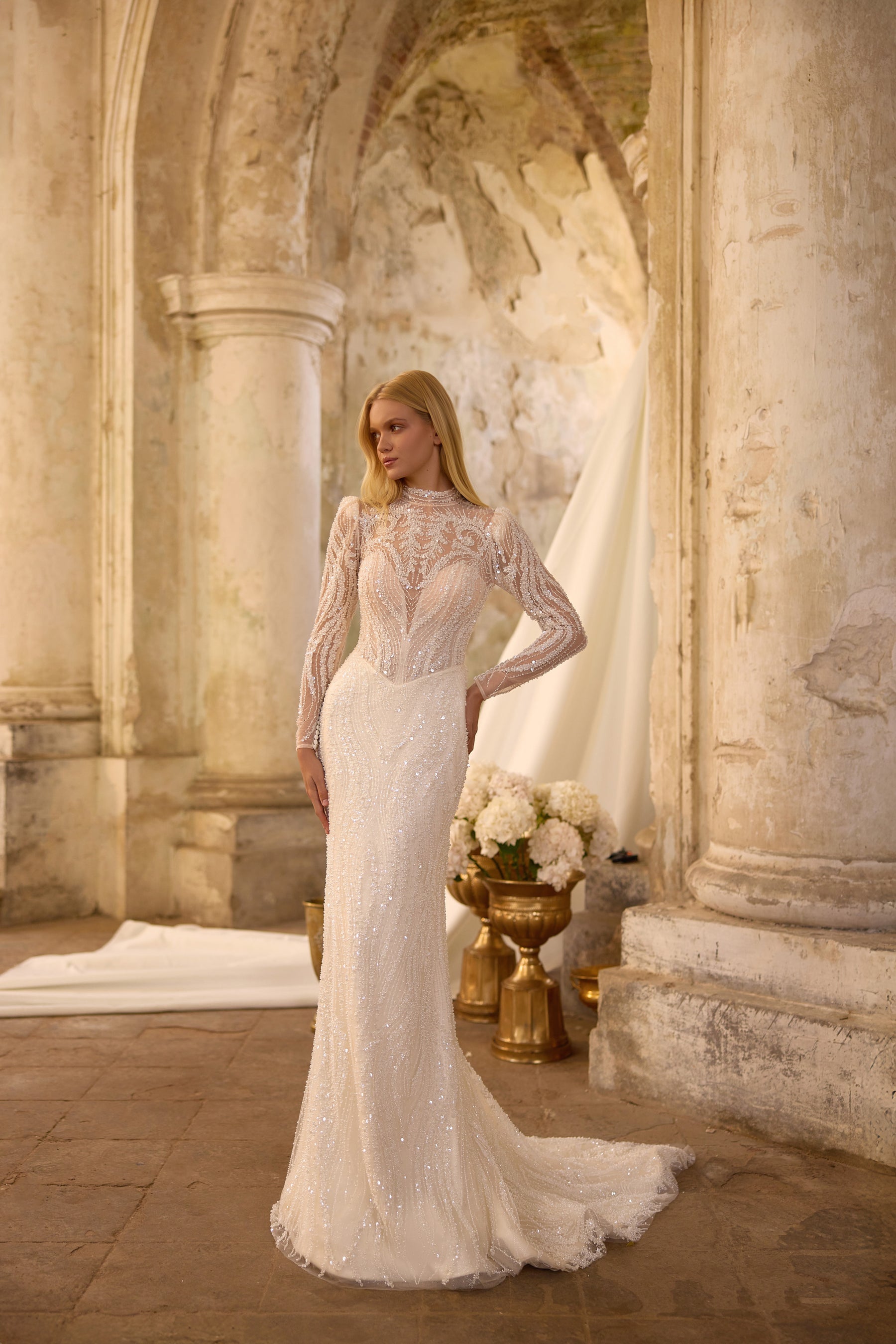 Fitted ivory sheath wedding dress covered in beadwork, with long lace sleeves and a high neckline