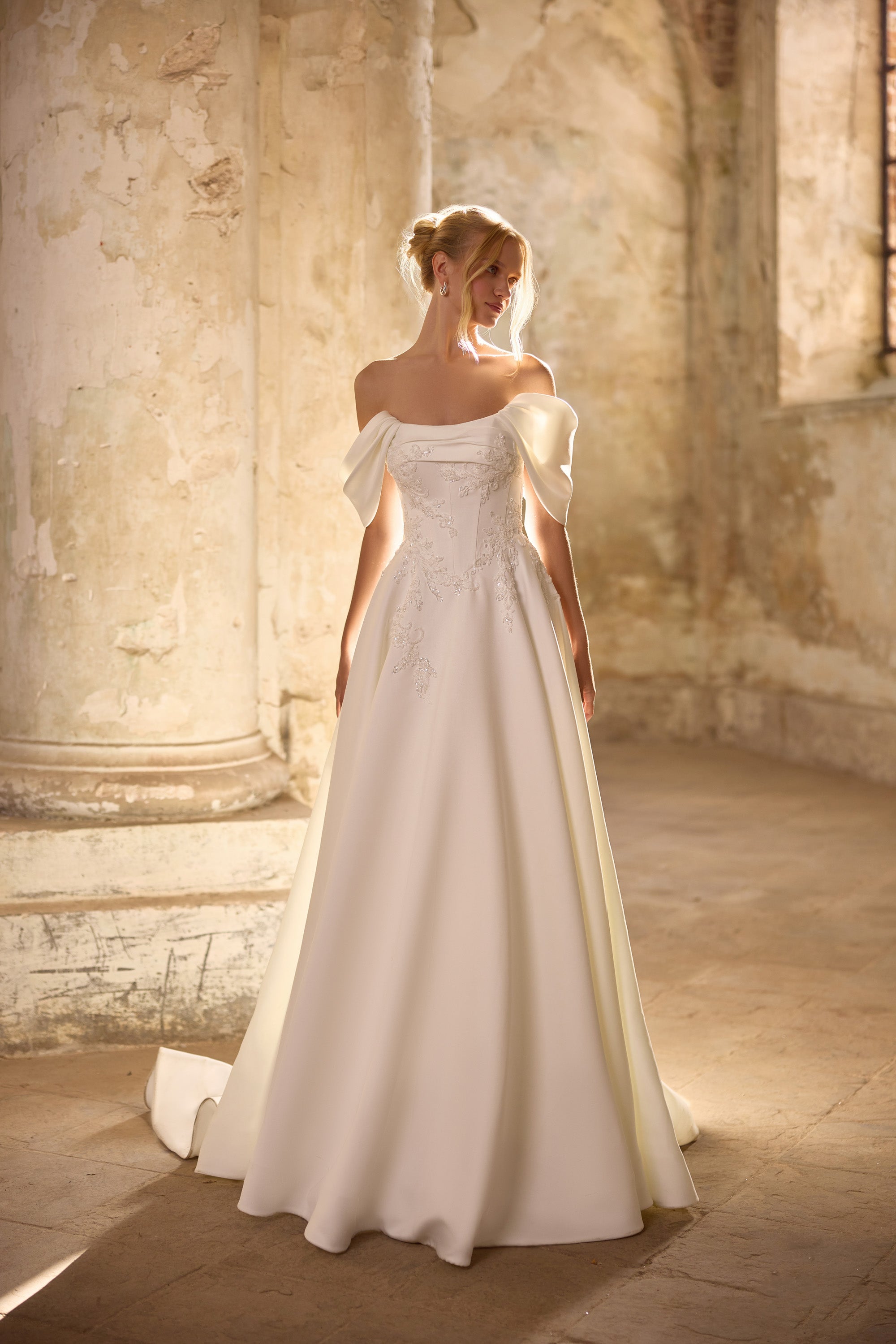 Ivory A-line wedding dress with an off-the-shoulder neckline, short sleeves, lace appliqués, and a train