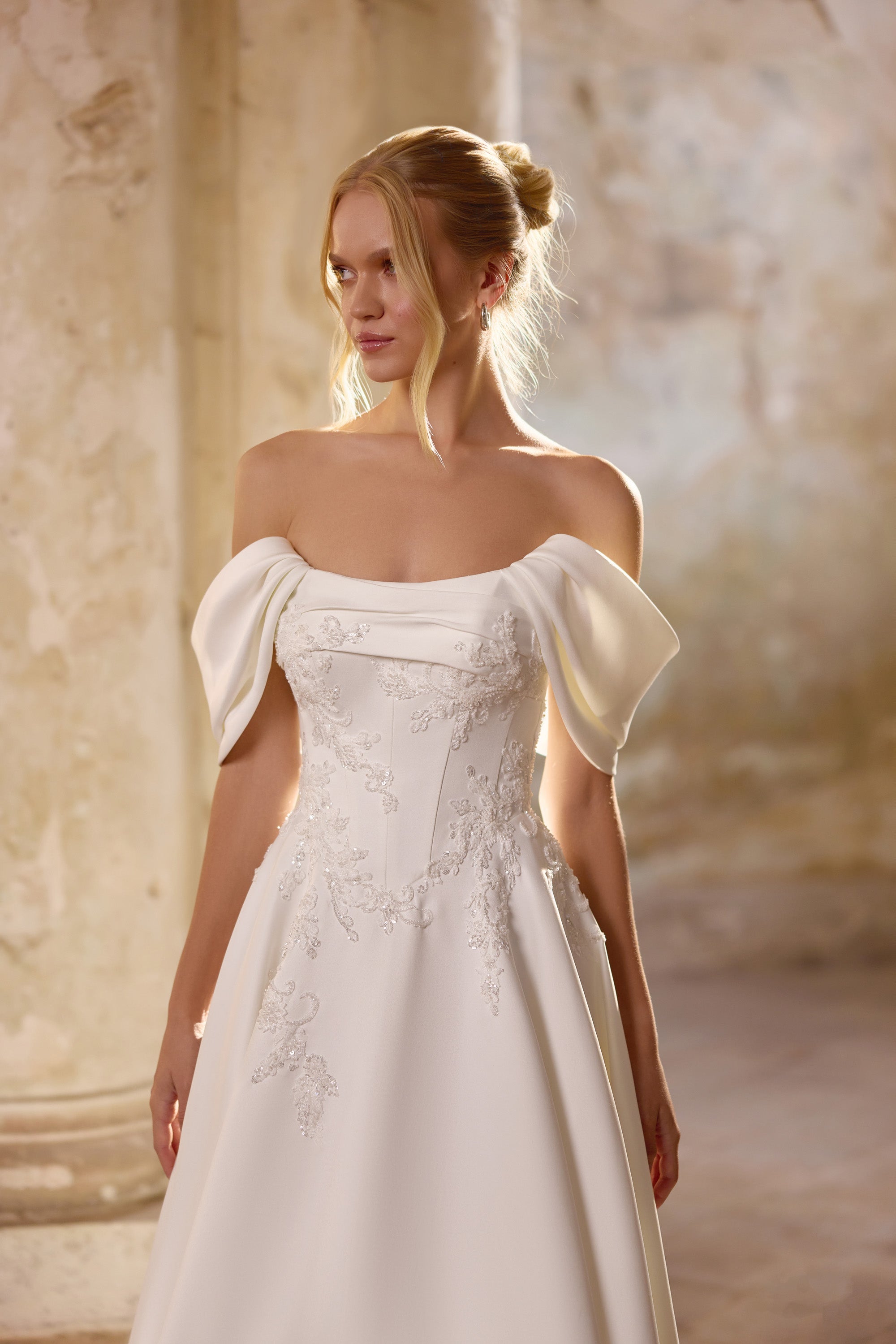 Ivory wedding dress with an off-the-shoulder neckline, draped short sleeves, and floral lace appliqués on the bodice