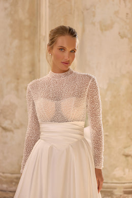 Close-up of the sheer beaded high-neck bodice and pleated waistband on an ivory wedding dress