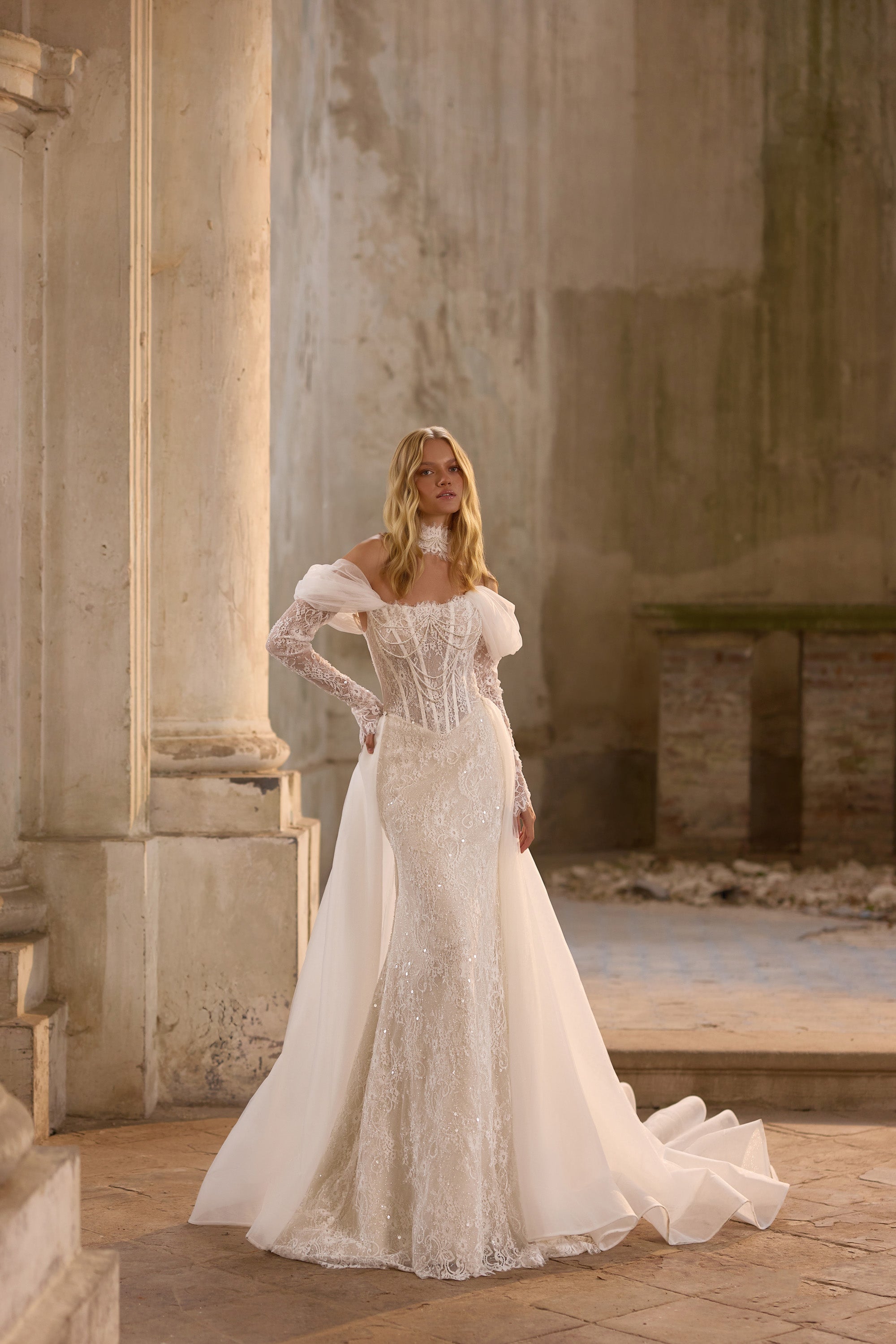 Ivory wedding dress with a beaded corset bodice, off-the-shoulder sleeves, and flowing overskirt