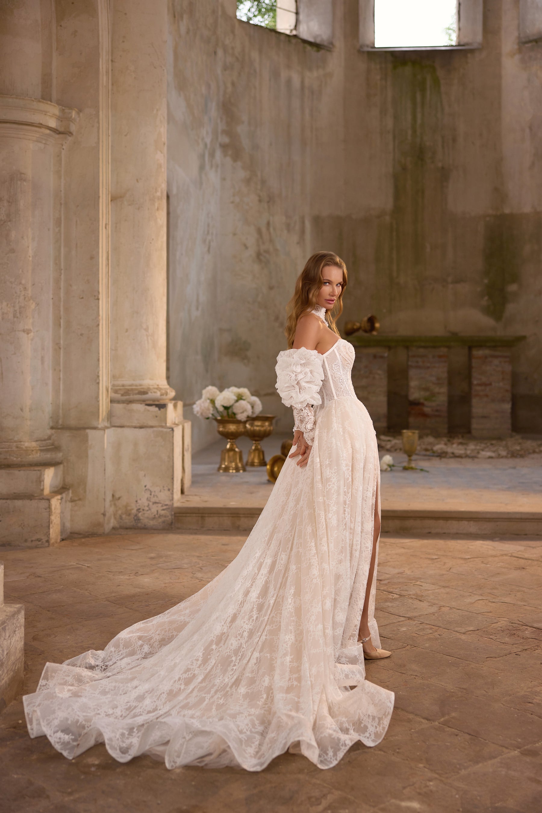 Side view of an ivory lace wedding dress with off-shoulder sleeves, a high slit, and a sweeping train