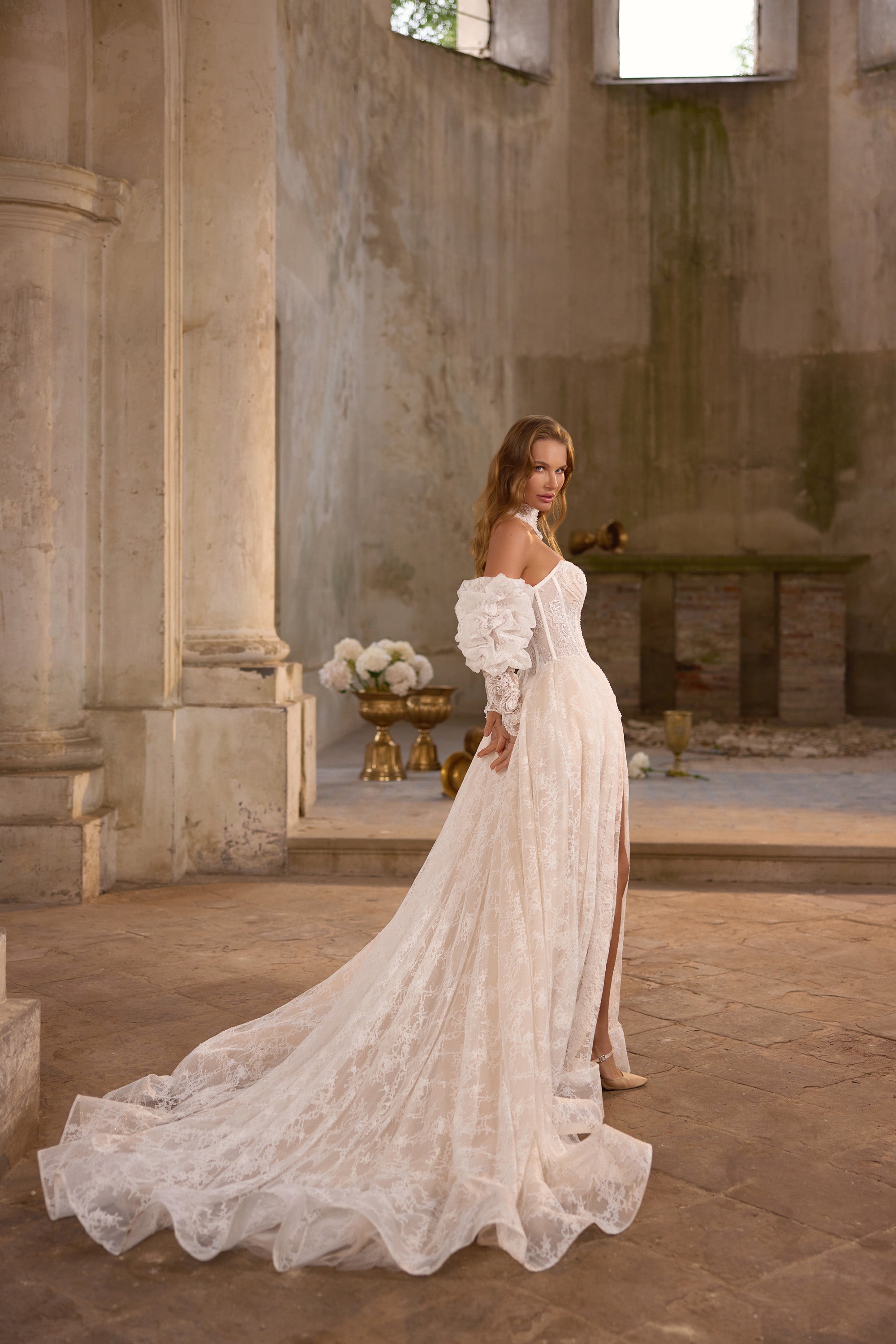 Side view of an ivory lace wedding dress with off-shoulder sleeves, a high slit, and a sweeping train
