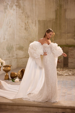 White beaded mermaid wedding dress with oversized ruffled sleeves and a flowing cape