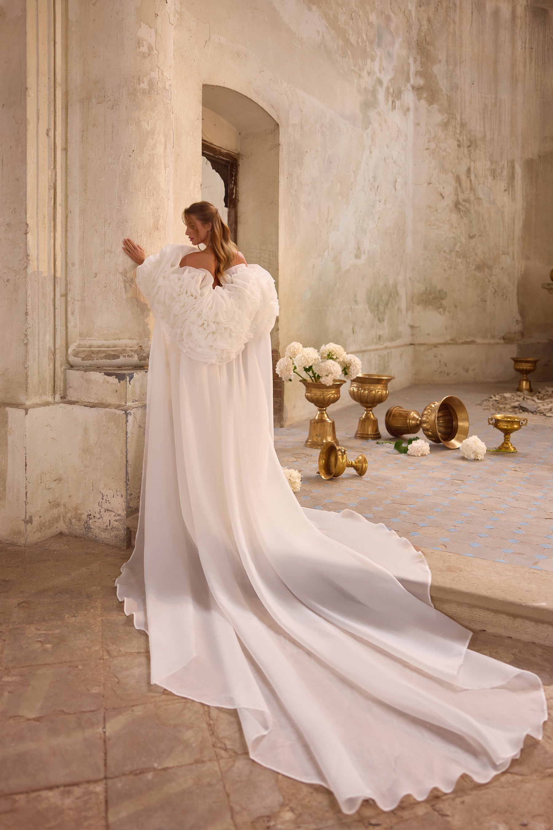 Back of a white wedding dress with a flowing cape and an exceptionally long, rippling train