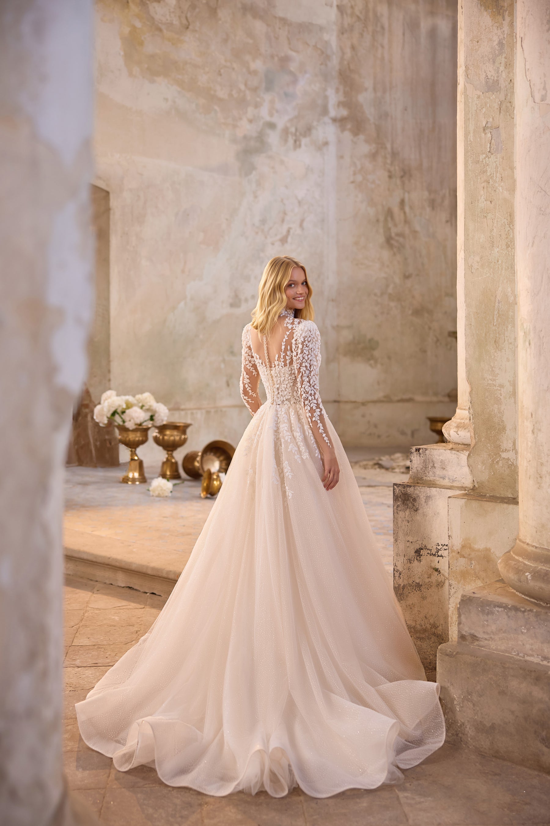 Ivory wedding dress showing a long-sleeved lace back, full flowing skirt, and extended train