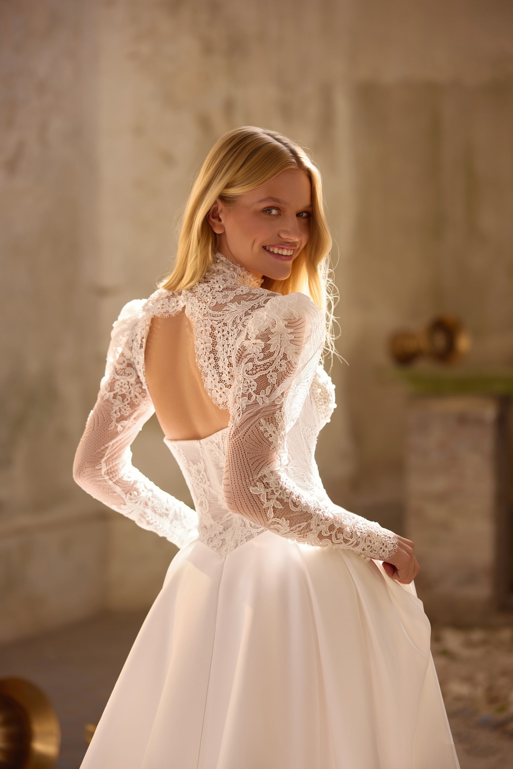 Ivory wedding dress with long lace sleeves, high neck, open back, and flowing A-line skirt