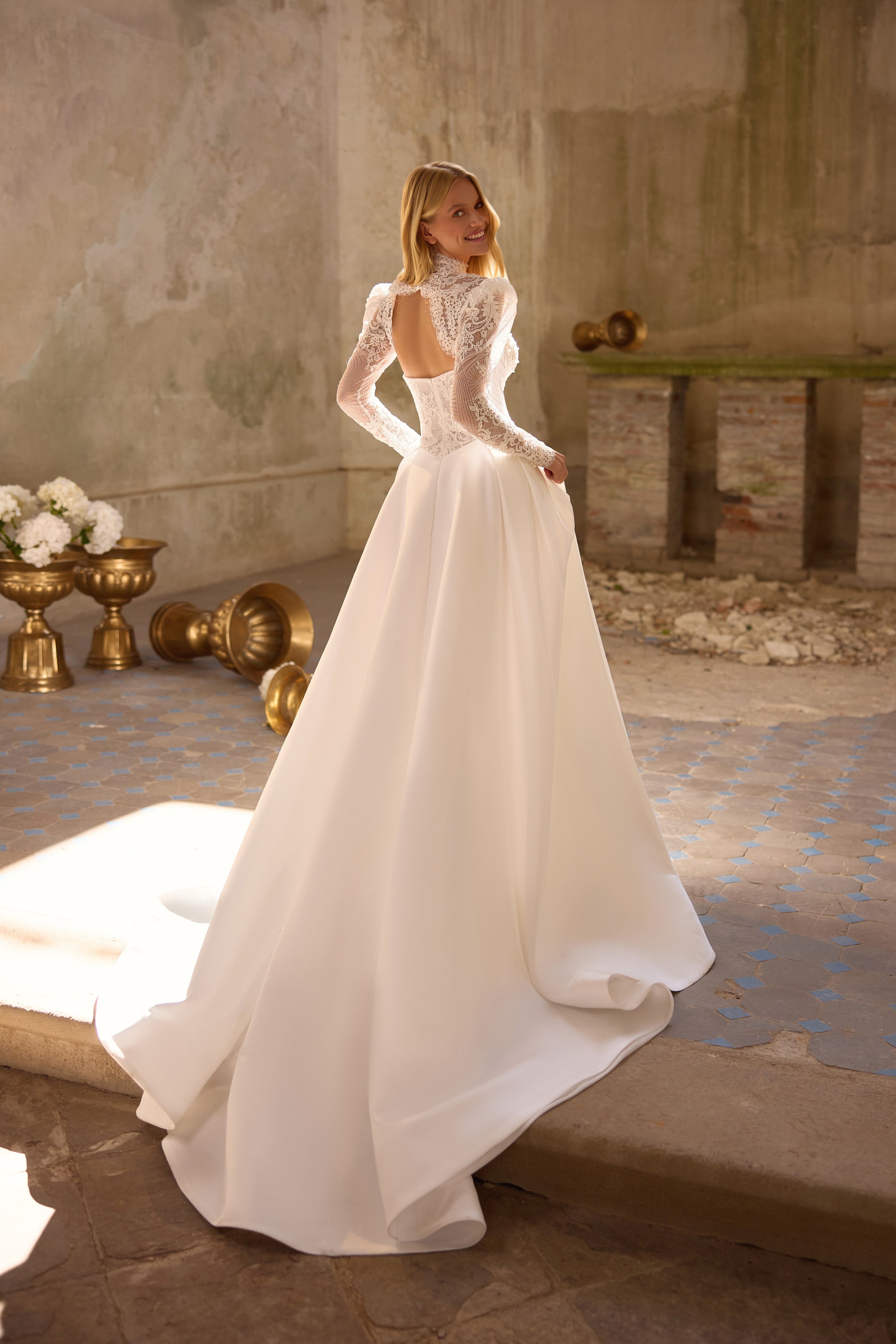 Ivory wedding dress showing an open lace back, long sleeves, smooth A-line skirt, and trailing train