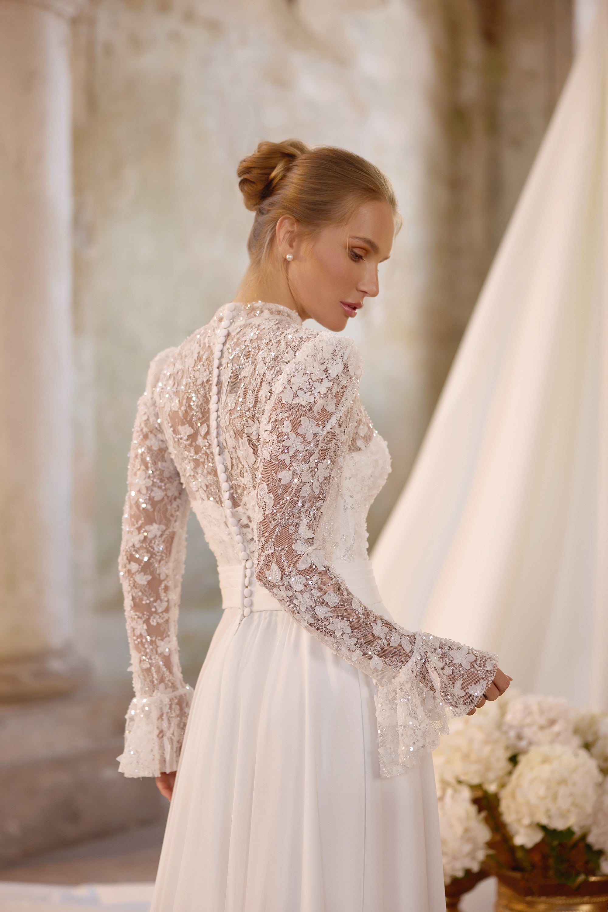 Ivory wedding dress with a sheer lace back, long floral lace sleeves, and covered buttons