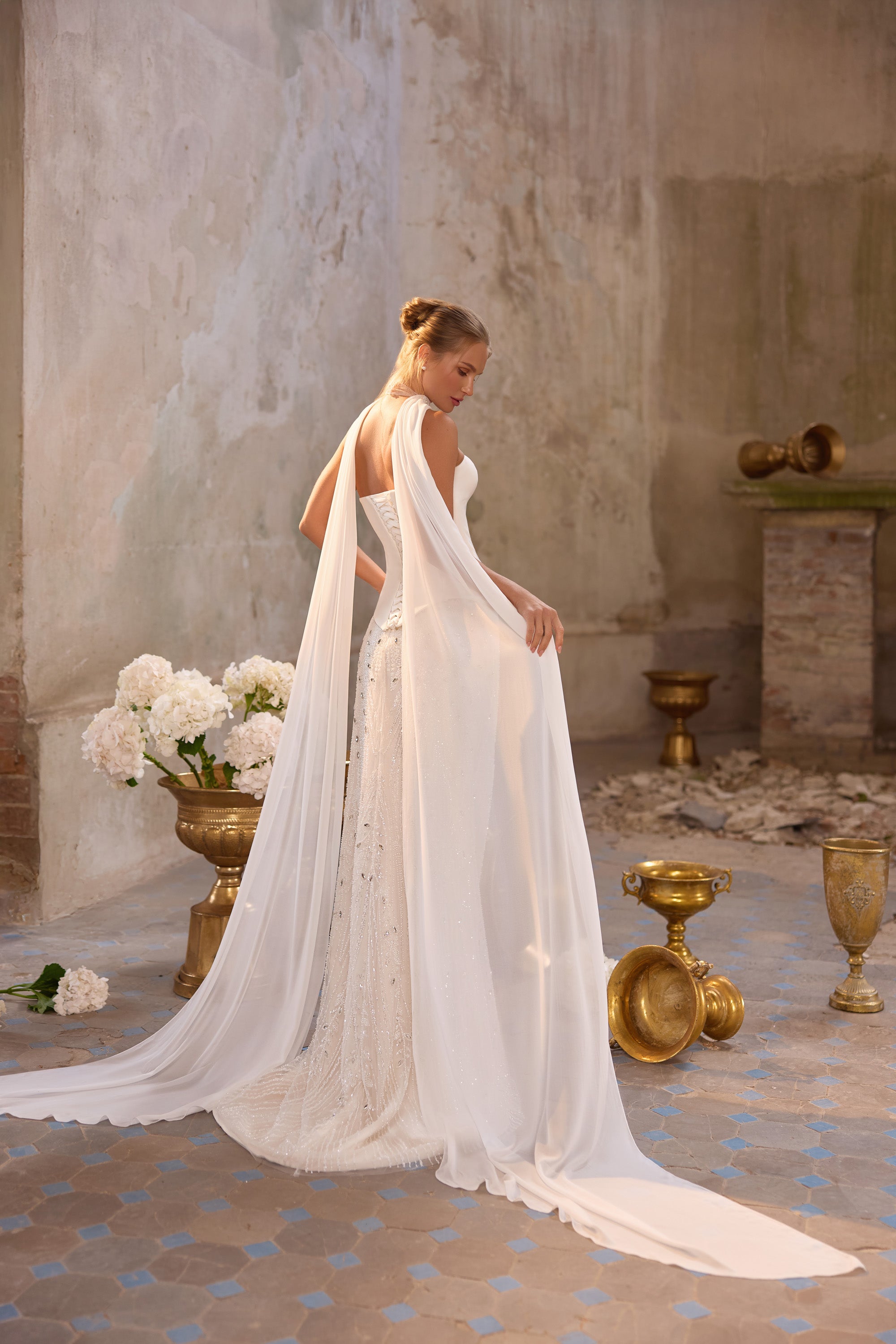 Open-back ivory wedding dress with a flowing chiffon cape and long trailing hem