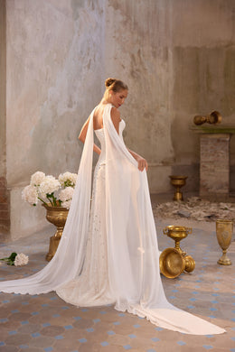 Open-back ivory wedding dress with a flowing chiffon cape and long trailing hem