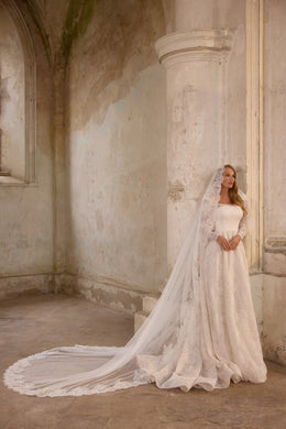 Ivory A-line wedding dress with a square neckline, long lace sleeves, glittering skirt, and cathedral veil