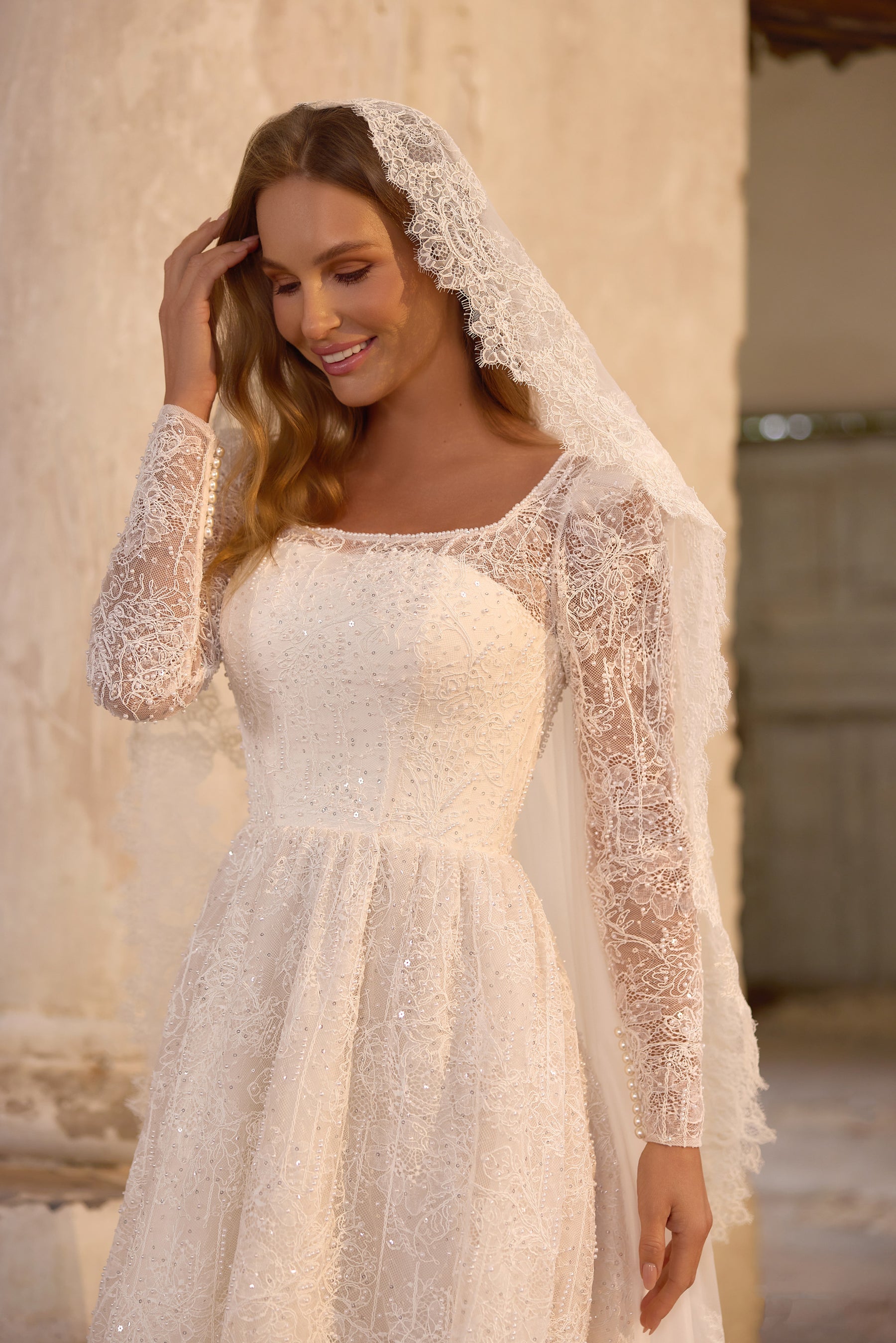 Close-up of an ivory wedding dress with a square neckline, beaded bodice, lace sleeves, and draped veil
