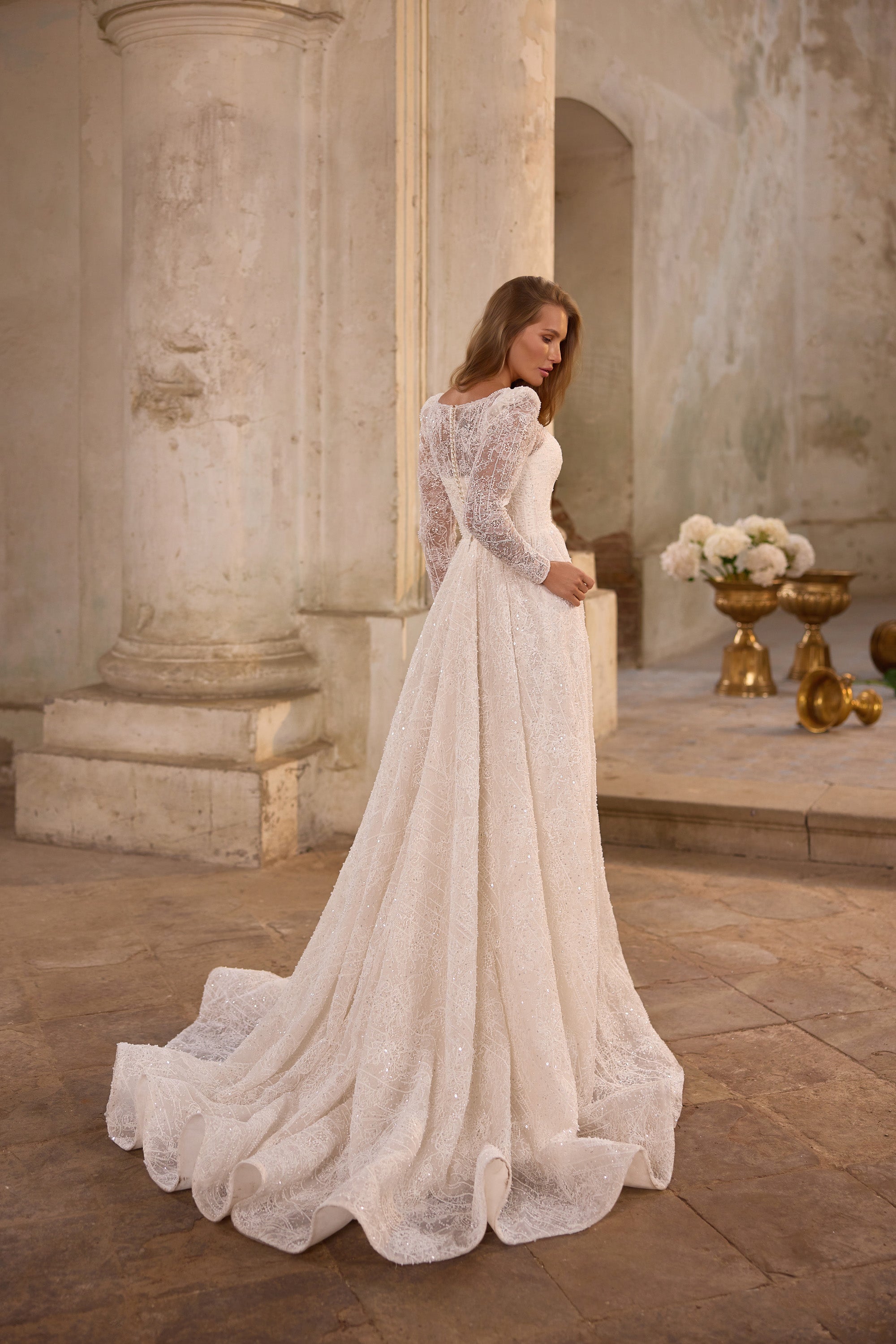 Rear view of an ivory wedding dress showing a lace-covered back, long sleeves, full skirt, and sweeping train