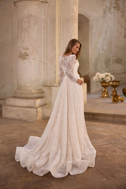 Rear view of an ivory wedding dress showing a lace-covered back, long sleeves, full skirt, and sweeping train