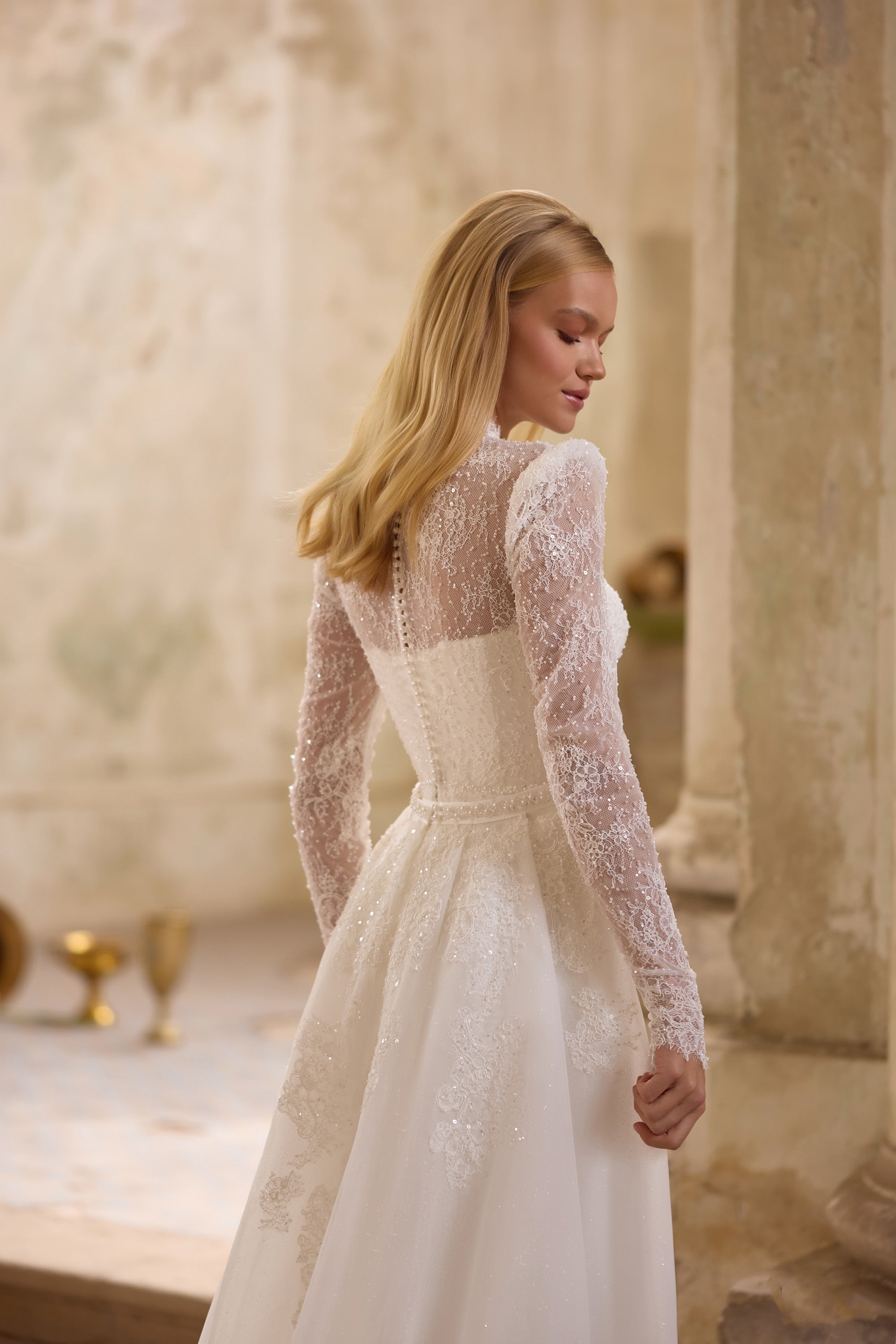 Ivory wedding dress with a sheer lace back, long lace sleeves, fitted waist, and flowing skirt